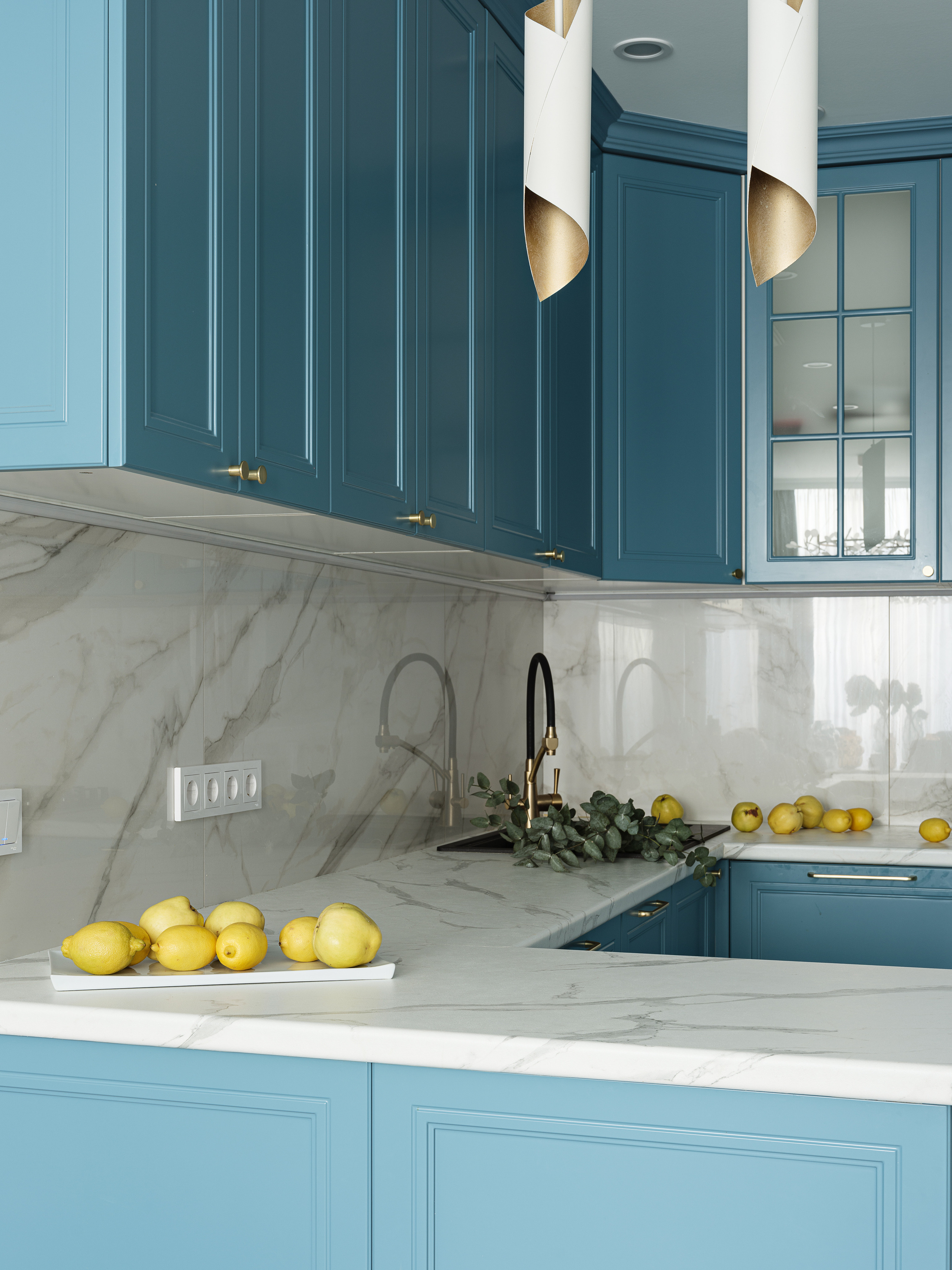Рабочая зона кухни с мраморным фартуком, золотыми смесителями и акцентом на яркие лимоны на белоснежной столешнице, стильный дизайн Светланы Олефиренко и Марии Морозовой, фото Сергея Денисенко, современный интерьер в светлых тонах.