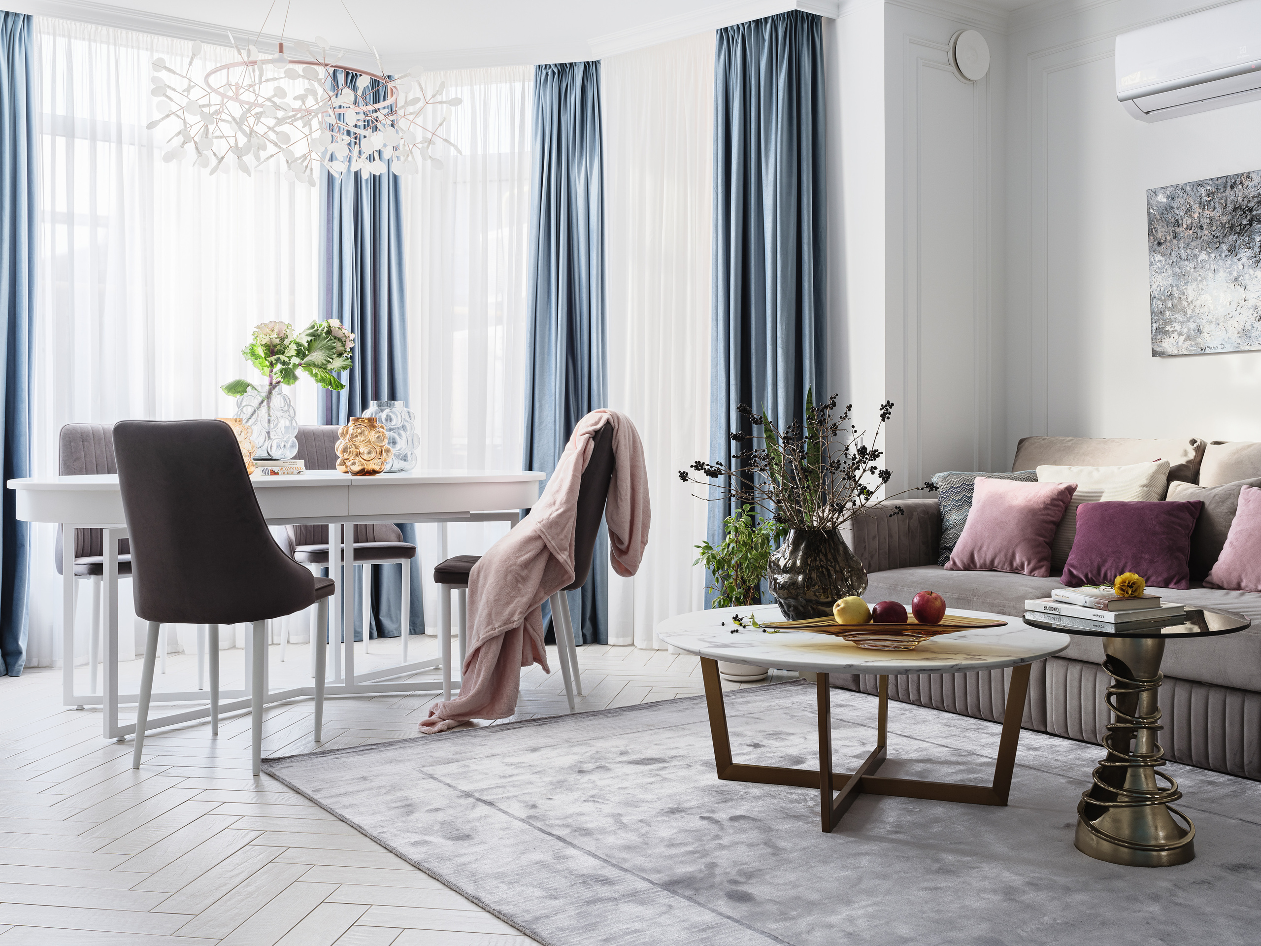 Современная гостиная-столовая в светлых тонах с серым диваном, кофейными столиками, голубыми шторами и элегантной люстрой. Авторское оформление от дизайнеров Светланы Олефиренко и Марии Морозовой, фотосъёмка Сергея Денисенко.