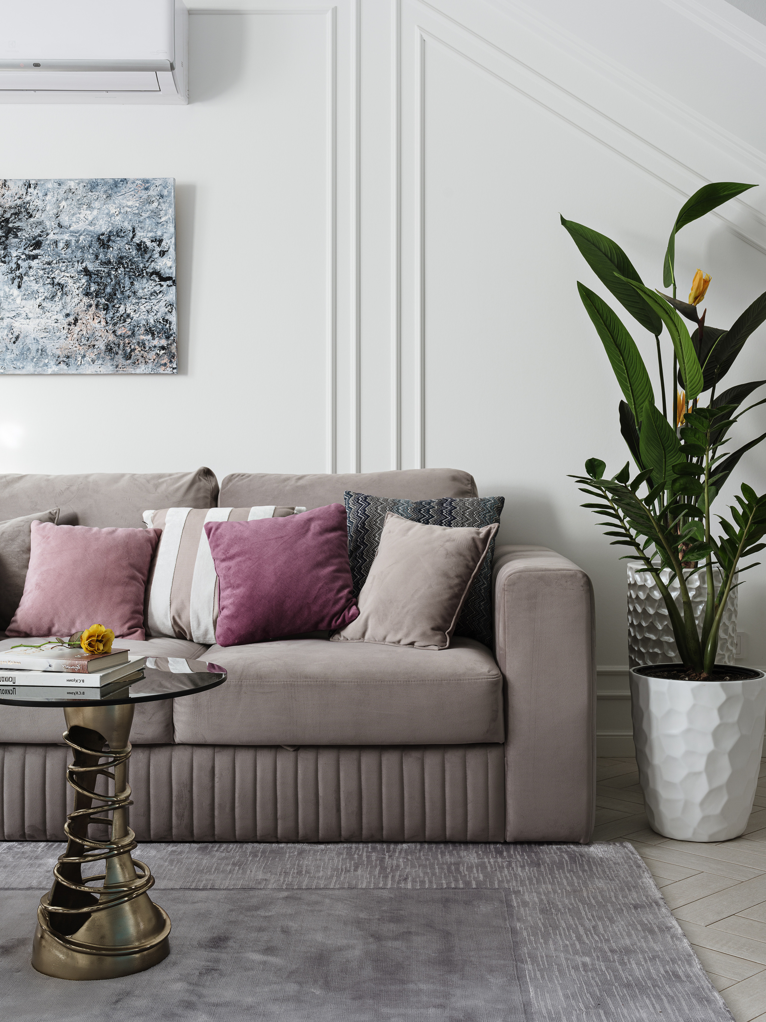 Современный уголок гостиной с мягким диваном, стильными подушками и крупным горшечным растением в белом кашпо на фоне геометричных стеновых панелей. Интерьер разработали дизайнеры Светлана Олефиренко и Мария Морозова, снимок Сергея Денисенко.