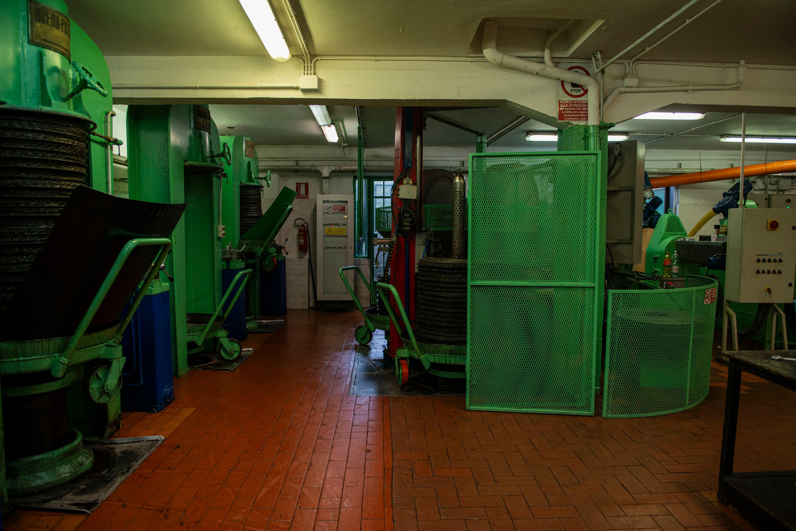 Промышленный цех по производству оливкового масла с зелеными машинами, оранжевой плиткой на полу и оборудованием для прессования и экстракции масла.