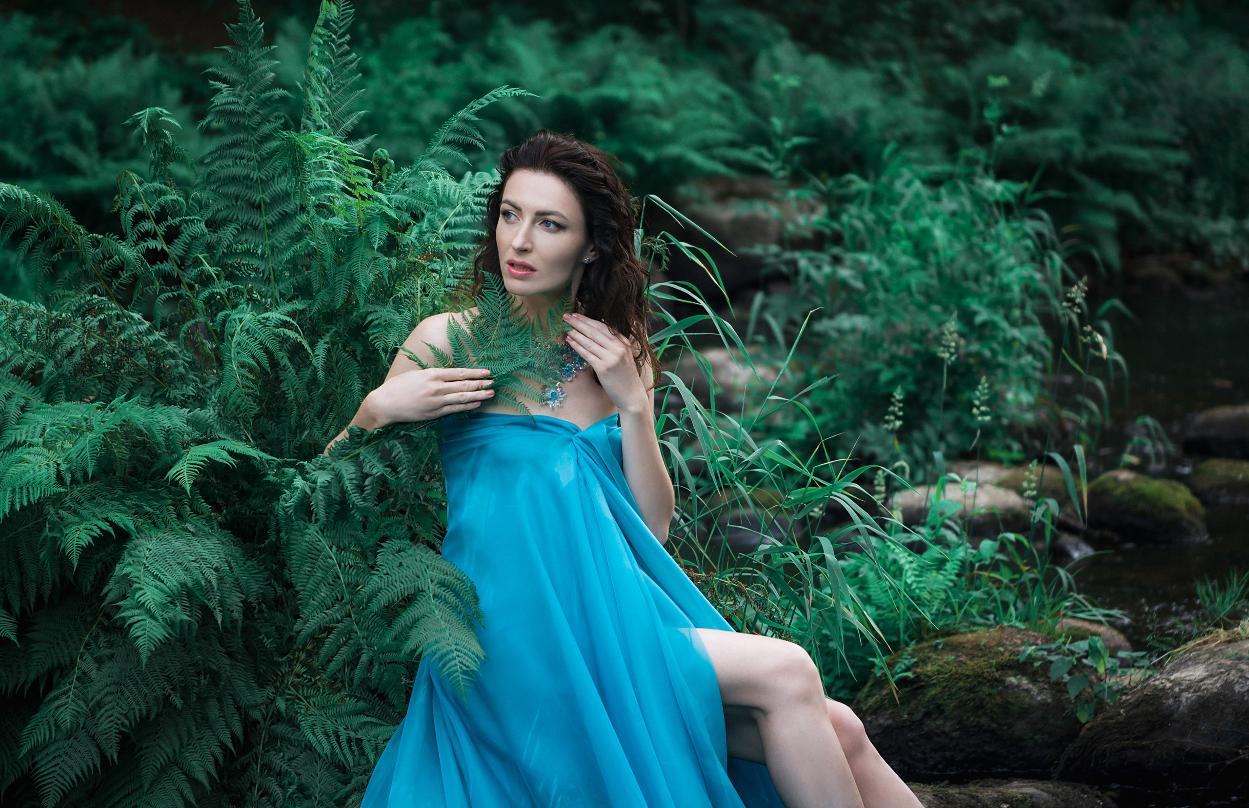 Девушка в голубом платье на камнях на берегу реки, рядом папоротник