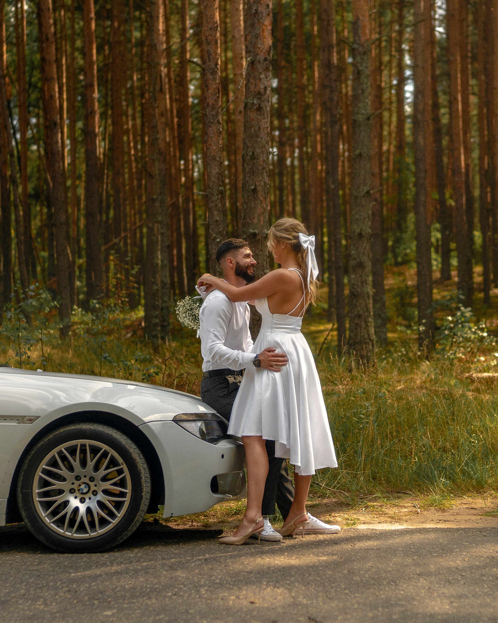 Молодожены обнимаются около автомобиля на природе