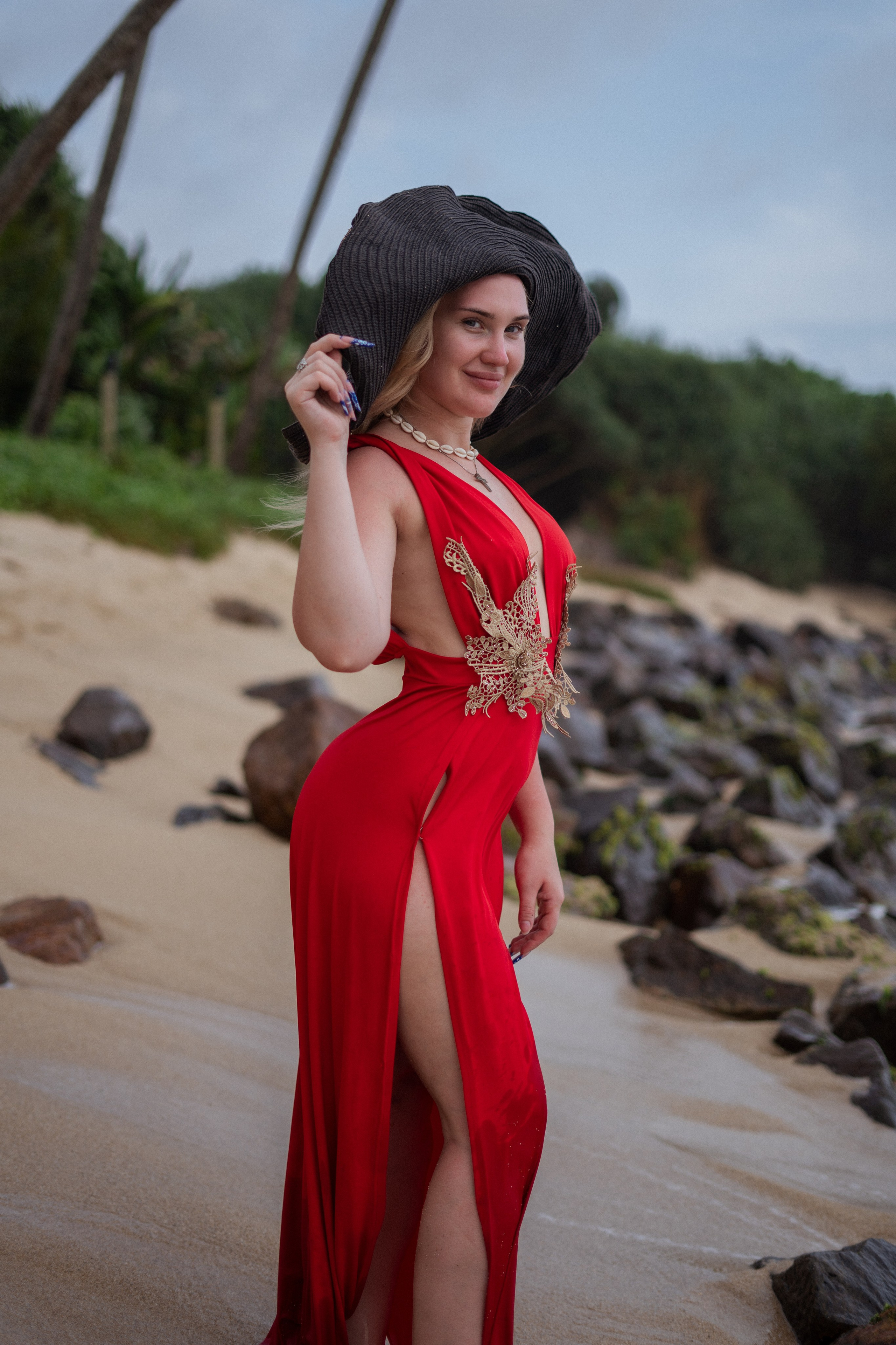 a beautiful blonde in a red dress standing barefoot on the sandy beach