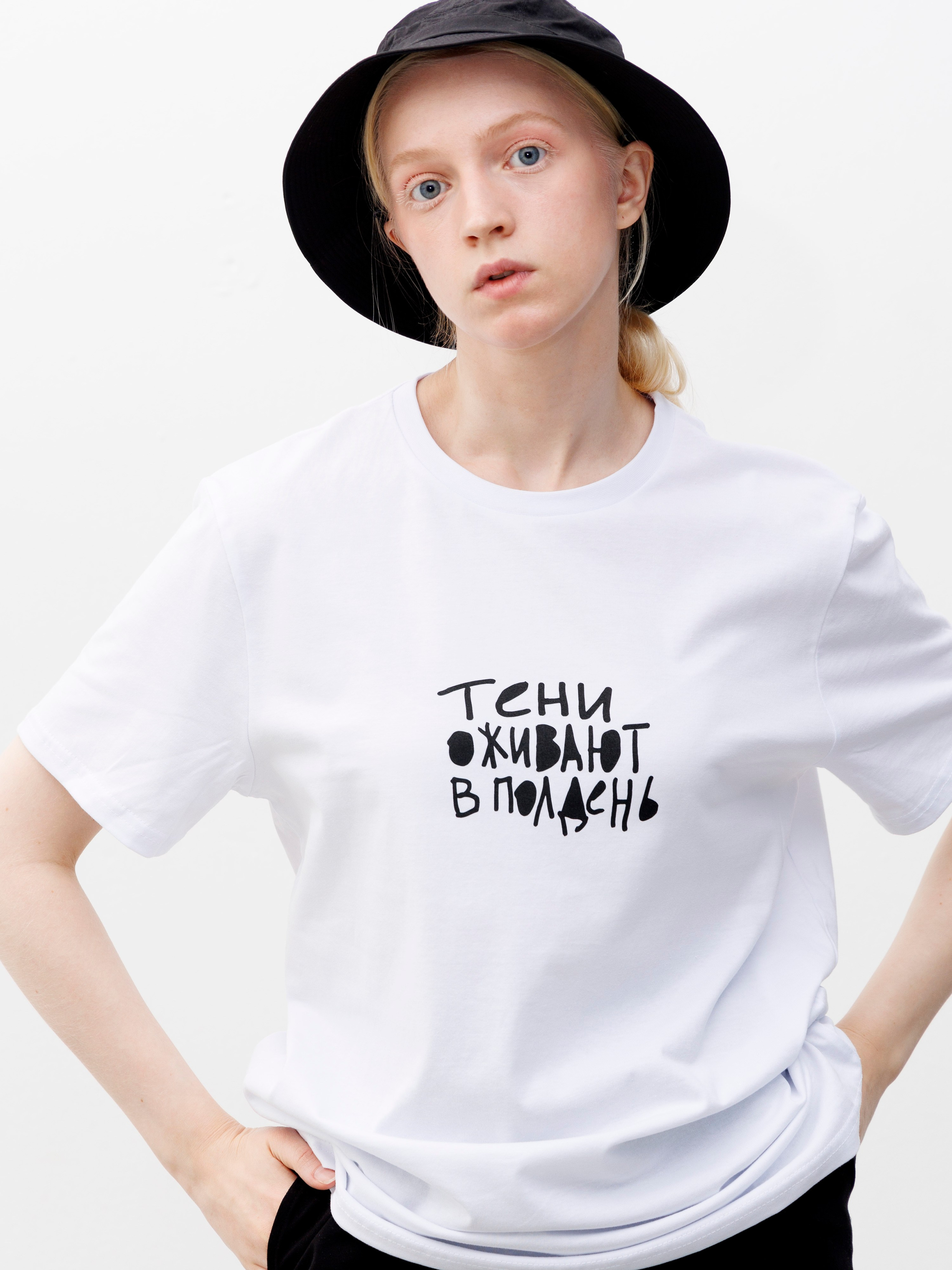 Девушка в черной панаме и белой футболке стоит на белом фоне