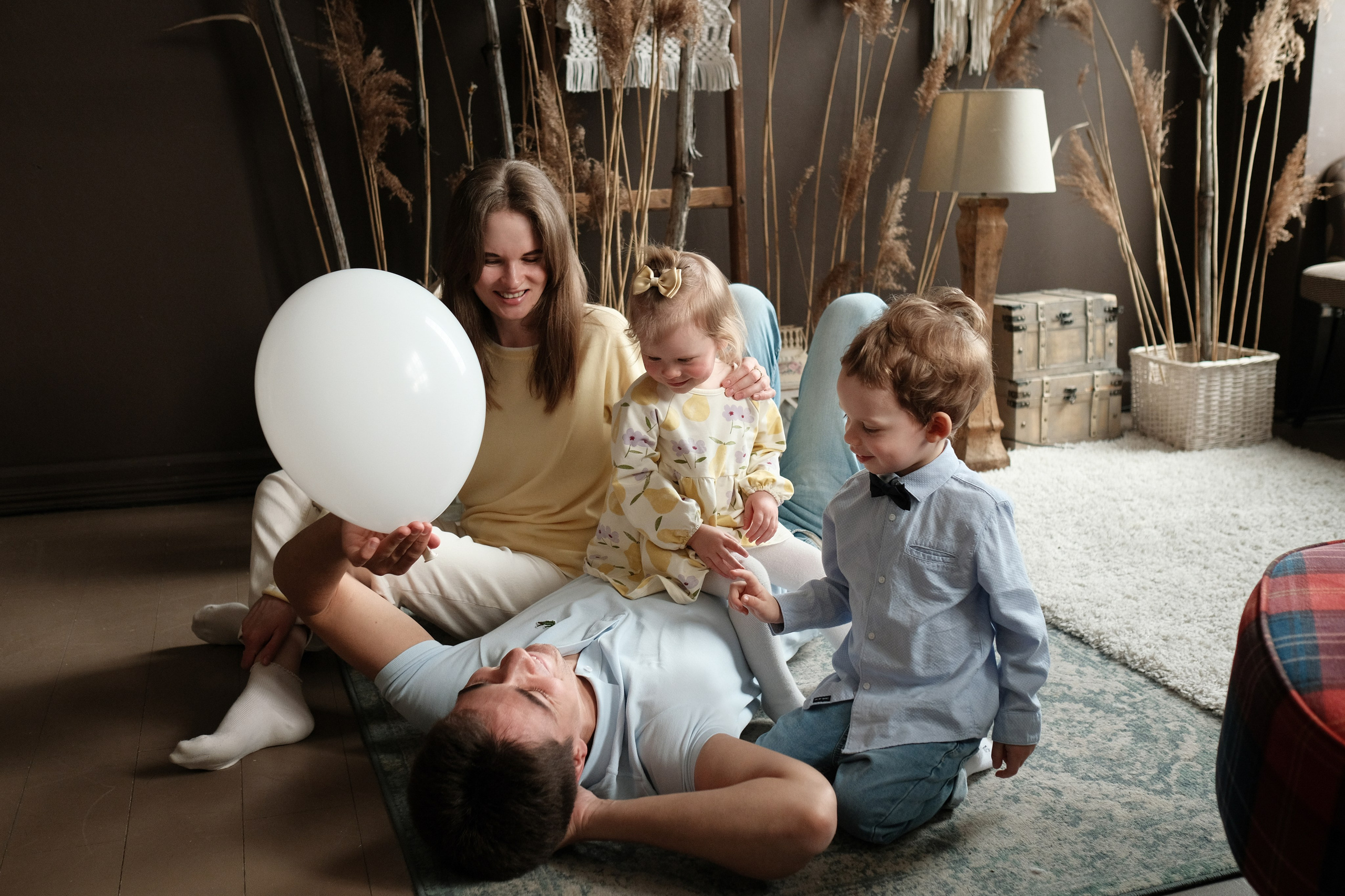 Семейная фотография в студии на полу, дочка сидит на папе, папа запускает шарик.