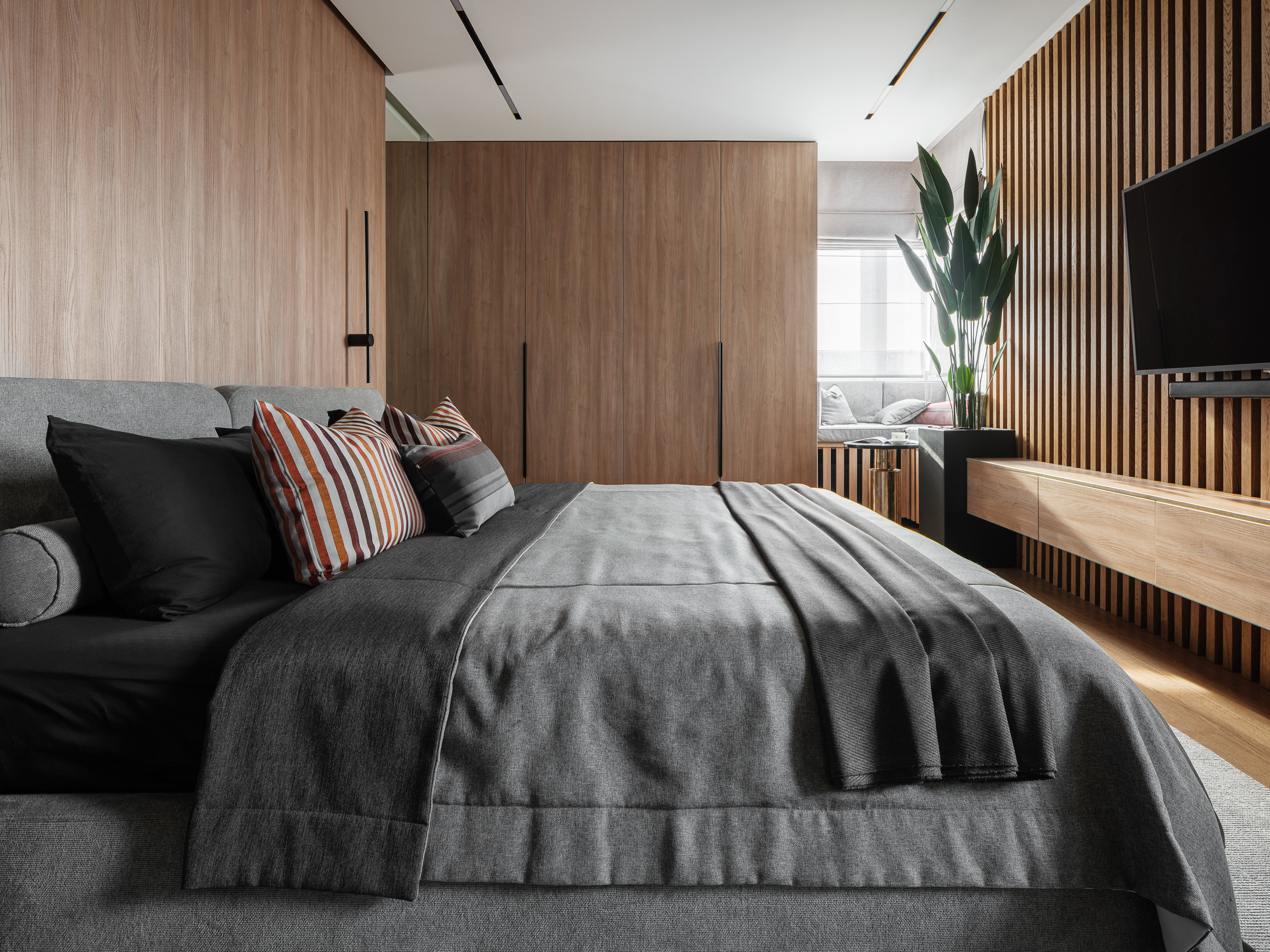 Просторная спальня с серым текстилем, декоративными подушками в полоску и деревянными панелями на стенах. Автор проекта Алёна Сверлова, фотограф Сергей Денисенко, современный уютный дизайн.