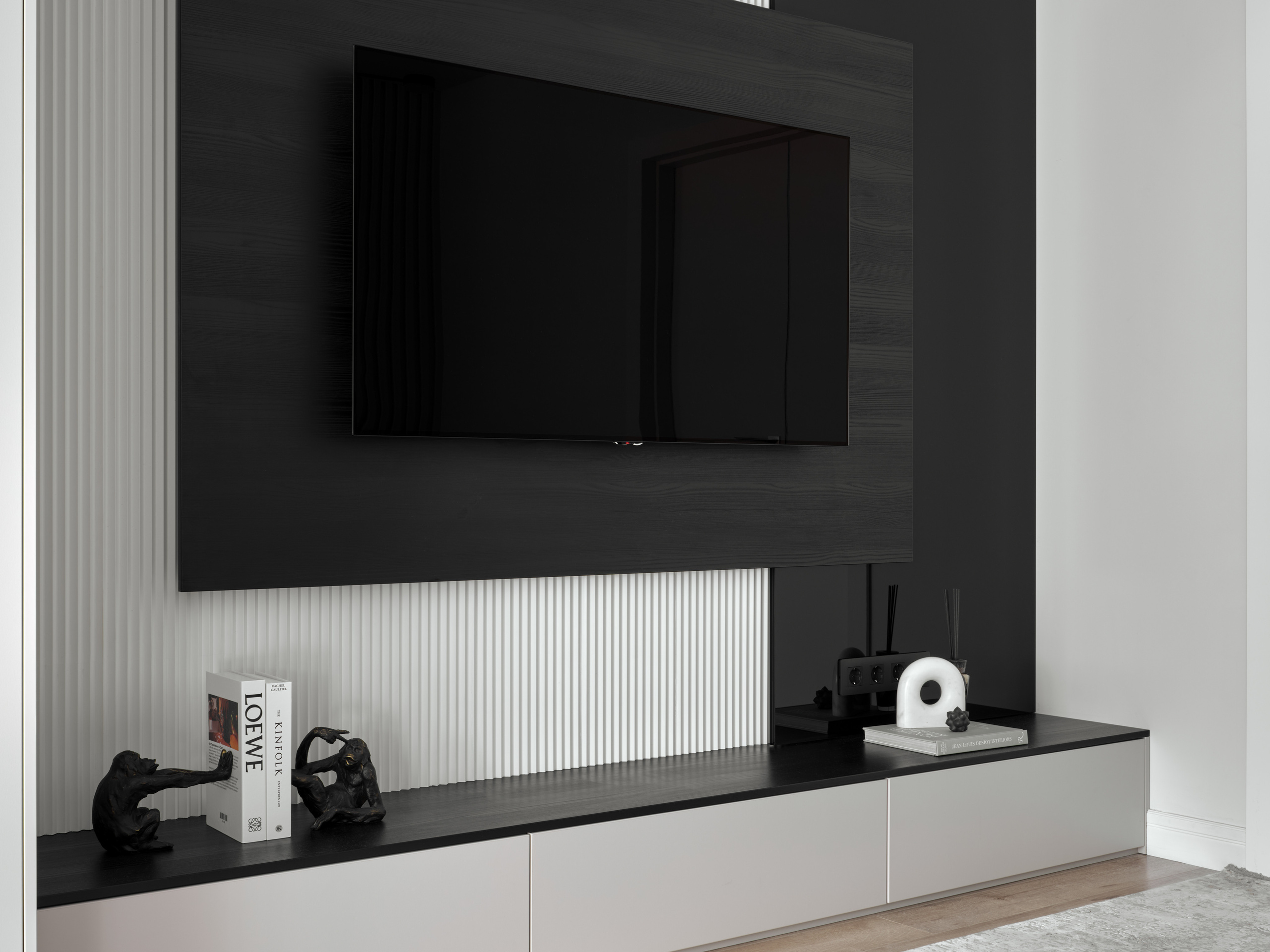 Минималистичная ТВ-зона с черной панелью, белыми рифлёными элементами и стильным декором на длинной тумбе. Дизайн выполнен Екатериной Мищенко, интерьер снят фотографом Сергеем Денисенко.
