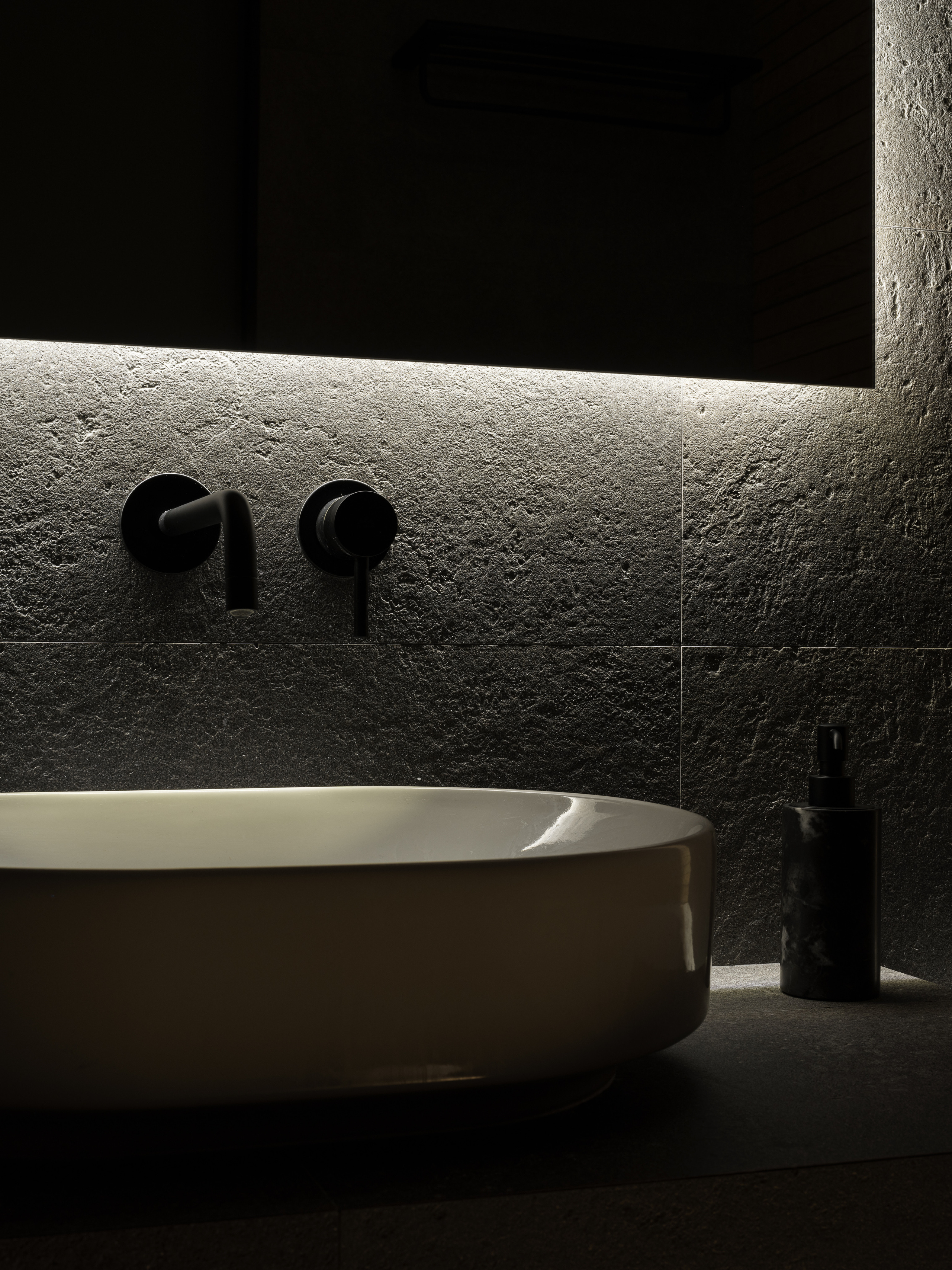 Крупный план овальной накладной раковины на каменной столешнице с черным настенным смесителем и подсветкой зеркала, стильный современный интерьер ванной комнаты с минималистичными акцентами, дизайнер Алёна Сверлова, фотограф Сергей Денисенко.