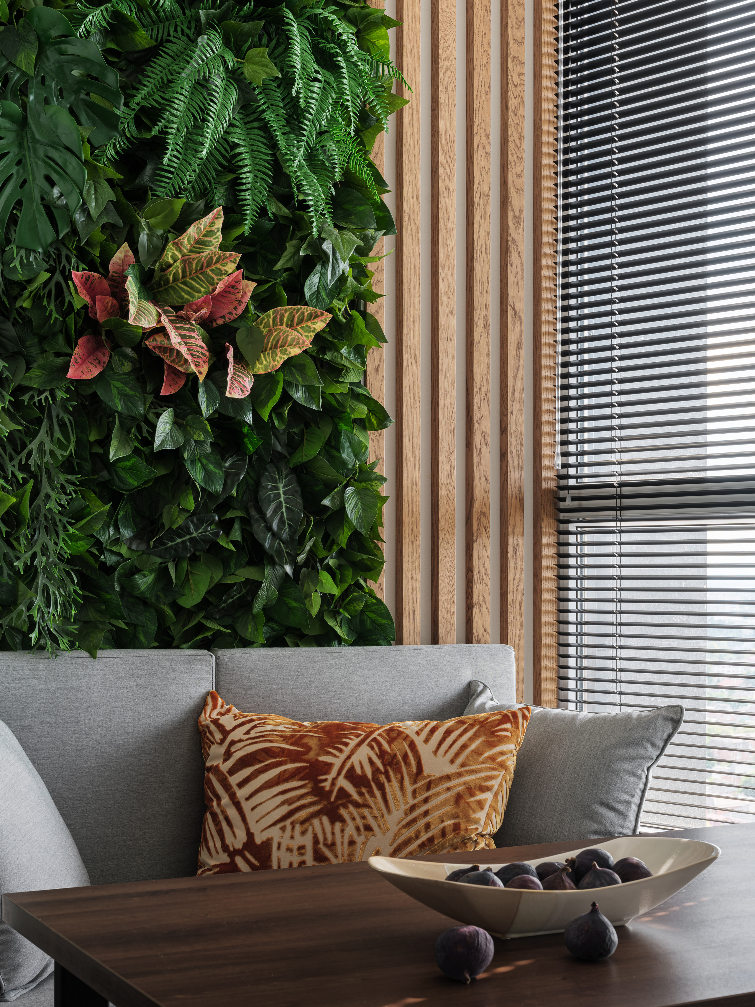 Интерьер зоны отдыха с вертикальным озеленением, серым диваном и декоративной подушкой с пальмовым принтом, акцент на натуральные текстуры и уют, современный стиль от дизайнера Алёны Сверловой, фото Сергей Денисенко.