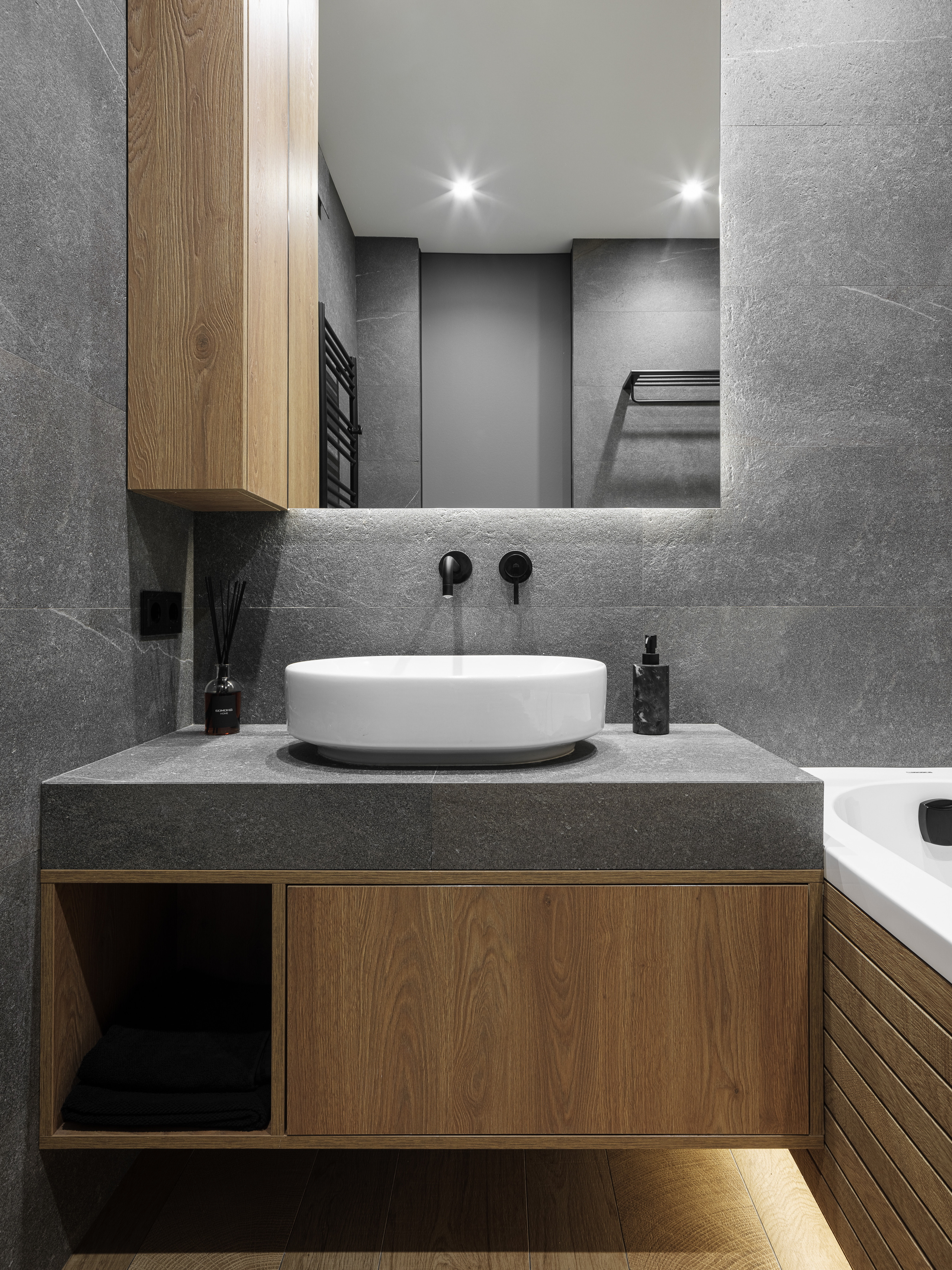 Интерьер ванной комнаты с серыми каменными плитами, деревянным шкафом и подсветкой под зеркалом, стильная белая раковина и аксессуары в минимализме, автор проекта Алёна Сверлова, профессиональная фотосъемка Сергей Денисенко.