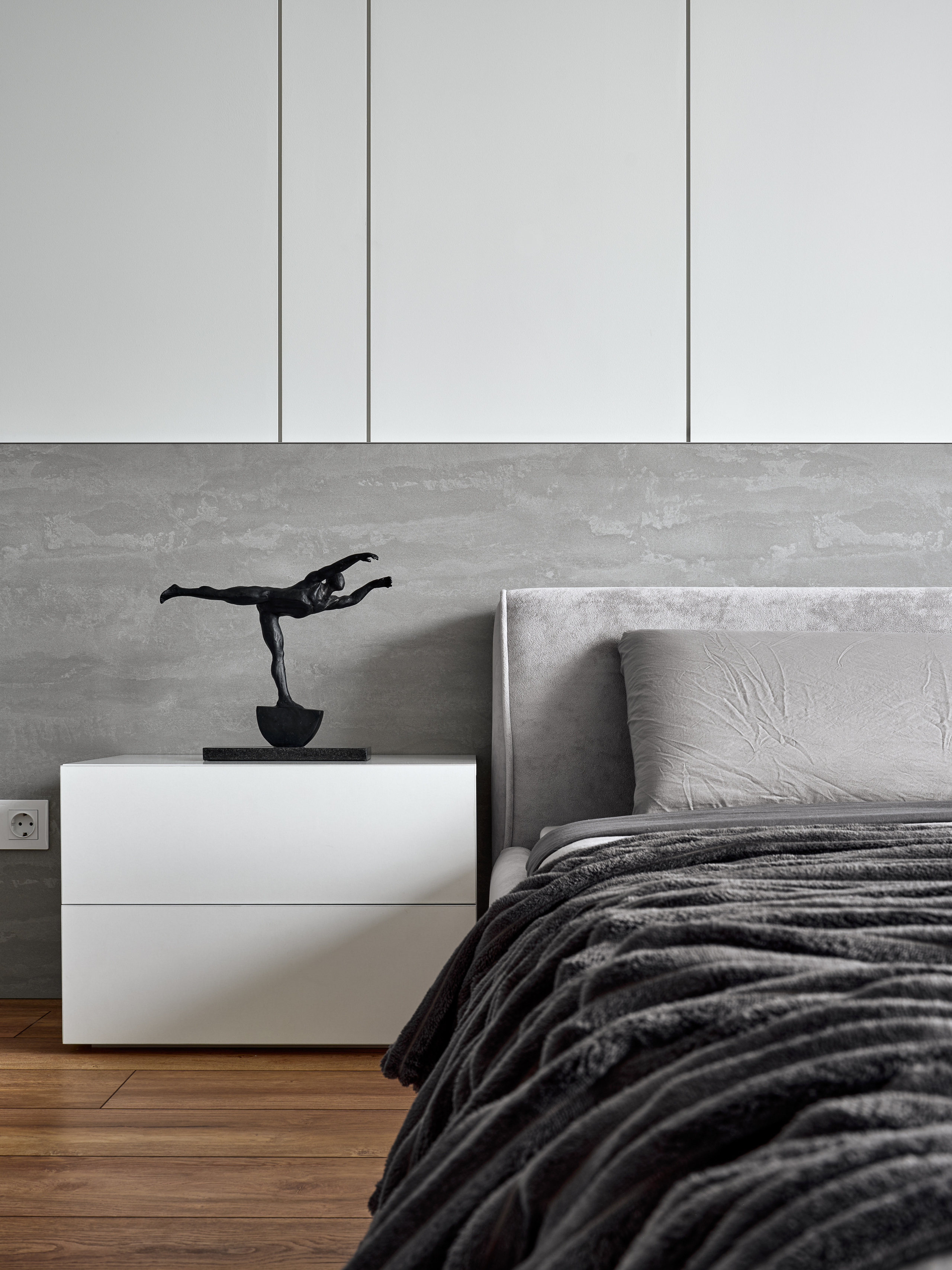 Деталь интерьера спальни с прикроватной тумбой белого цвета и скульптурой в стиле модерн на фоне серой текстурной стены, дизайн Андрея Нелень и Екатерины Проскуряковой, стилистика Алины Нелень, автор фото — Сергей Денисенко.