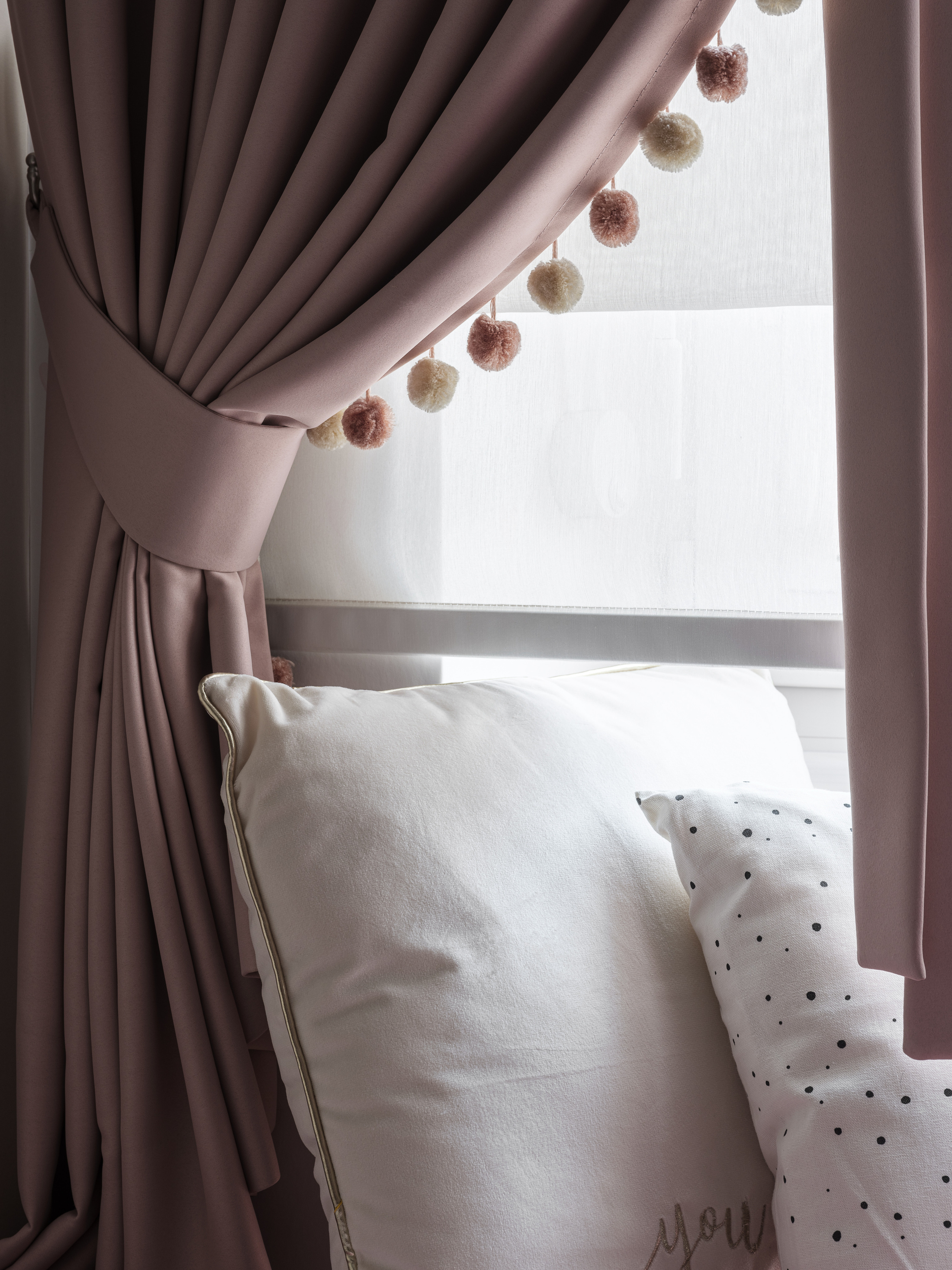 Уютный интерьер спальни в нежных тонах с розовыми шторами на подхвате и декоративными помпонами, акцент на белых подушках с принтом. Дизайнер Алёна Сверлова, фотограф Сергей Денисенко, современный стиль.