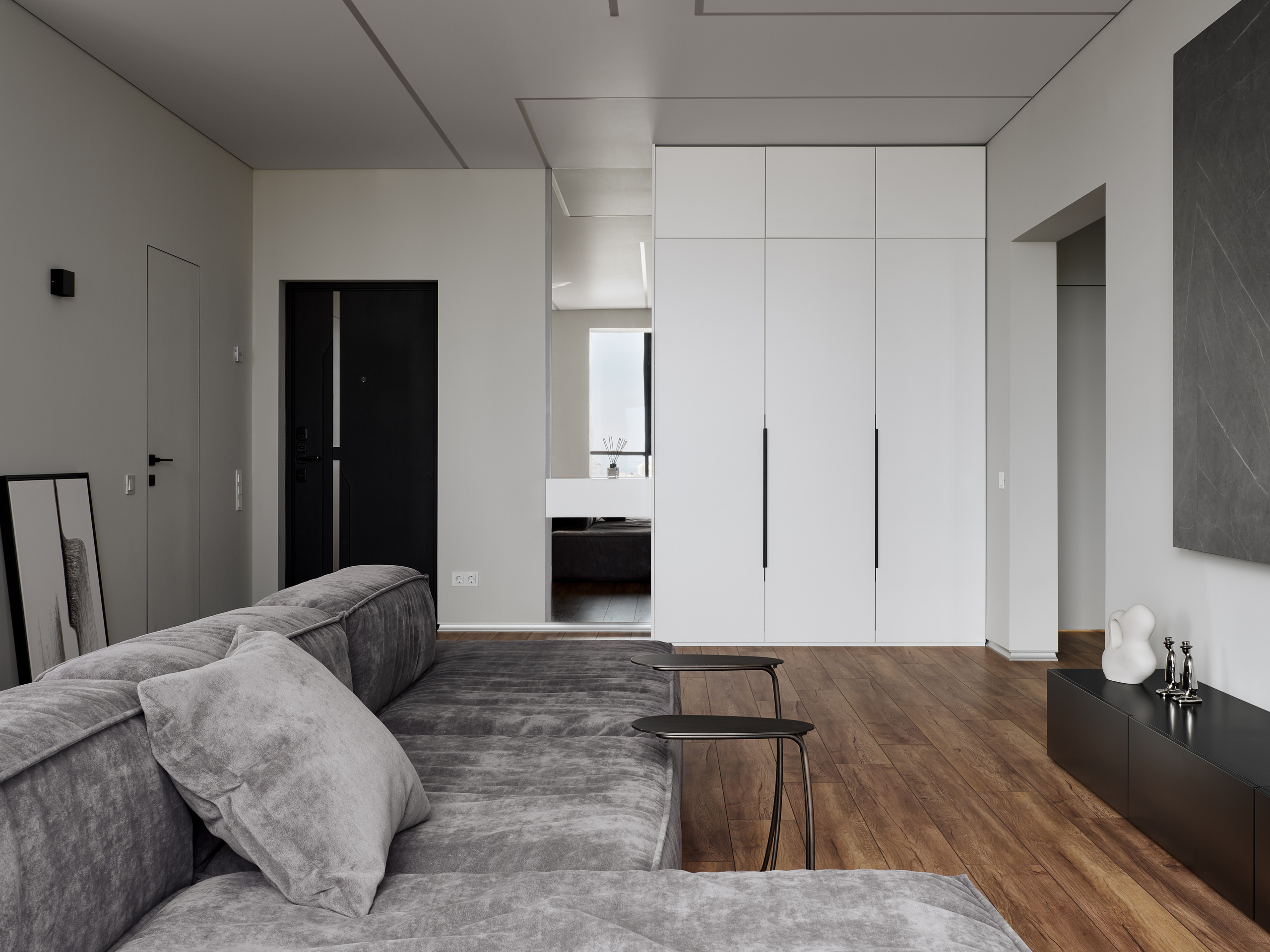 Просторная гостиная с большим серым диваном, встроенными белыми шкафами и деревянным полом в минималистичном стиле, интерьер от Андрея Неленя и Екатерины Проскуряковой, гармония деталей от Алины Нелень, фото Сергея Денисенко.