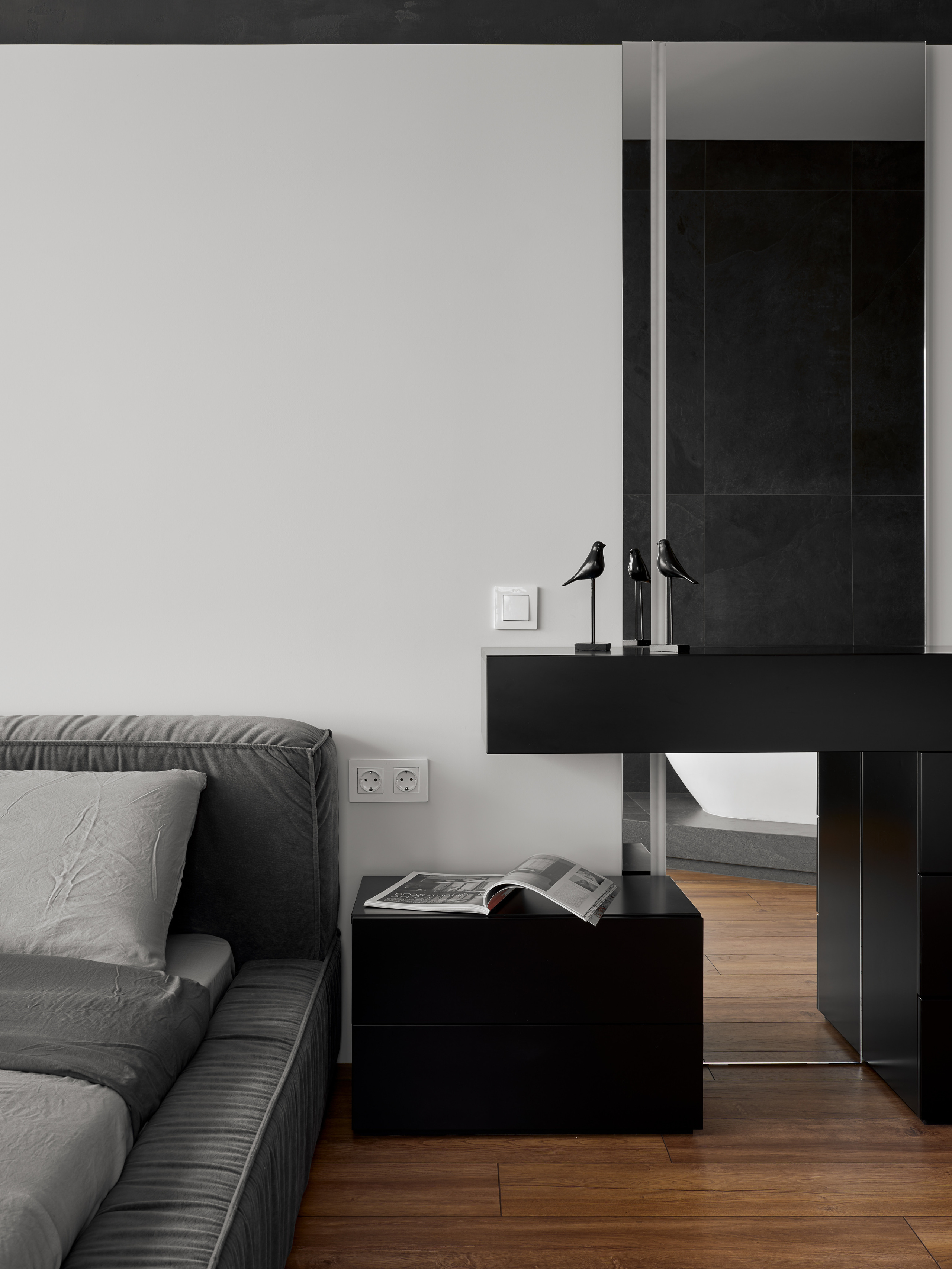 Фрагмент спальни с серым текстильным изголовьем, черной прикроватной тумбой и минималистичным туалетным столиком с зеркалом, интерьер создан Андреем Нелень и Екатериной Проскуряковой, стилист Алина Нелень, фотограф Сергей Денисенко.