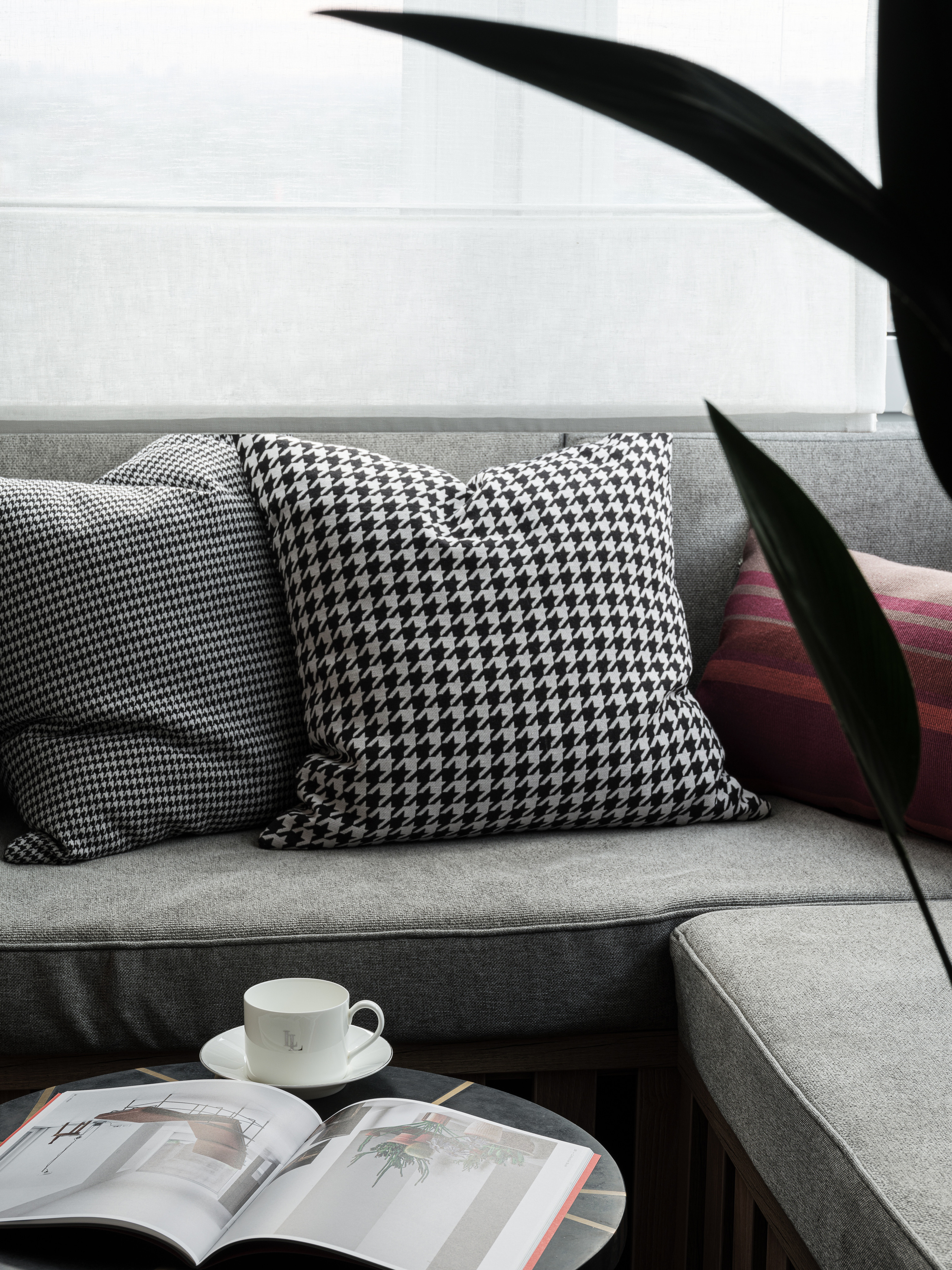 Стильный интерьер гостиной с серым диваном, декоративными подушками в клетку и чашкой на журнальном столике. Дизайнер Алёна Сверлова, фотограф Сергей Денисенко, гармония комфорта и современности.