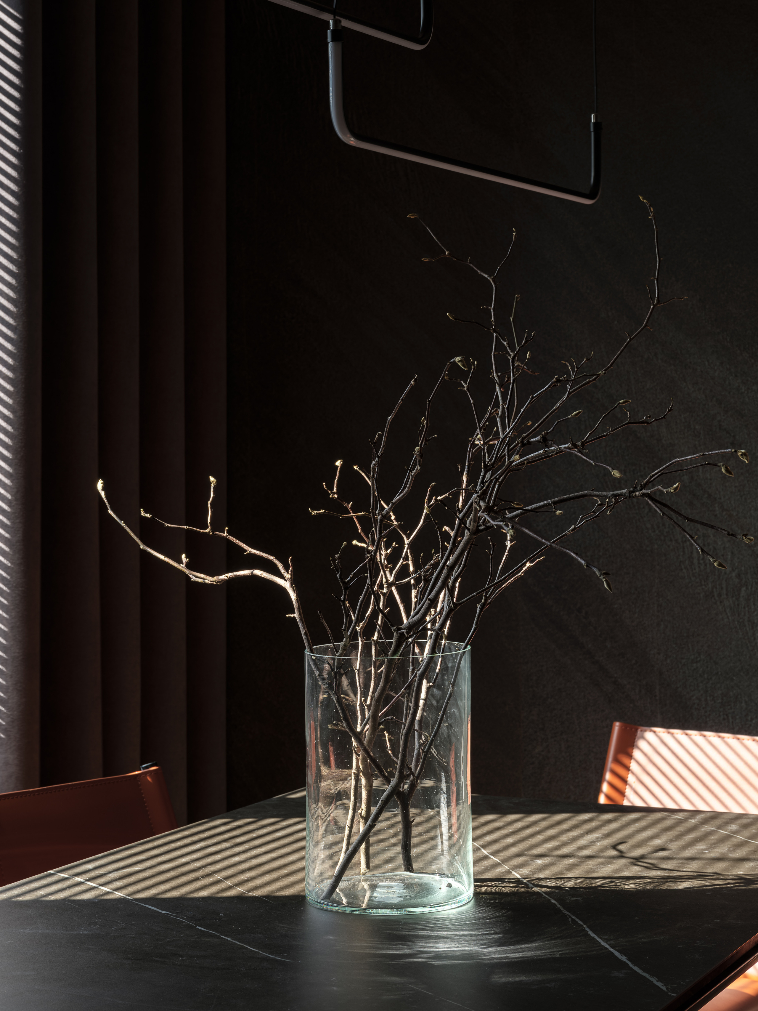 Минималистичная композиция с ветками в прозрачной стеклянной вазе на чёрном столе в столовой, стильные тени от жалюзи, современный интерьер в авторском исполнении дизайнера Алёны Сверловой, фото Сергей Денисенко.