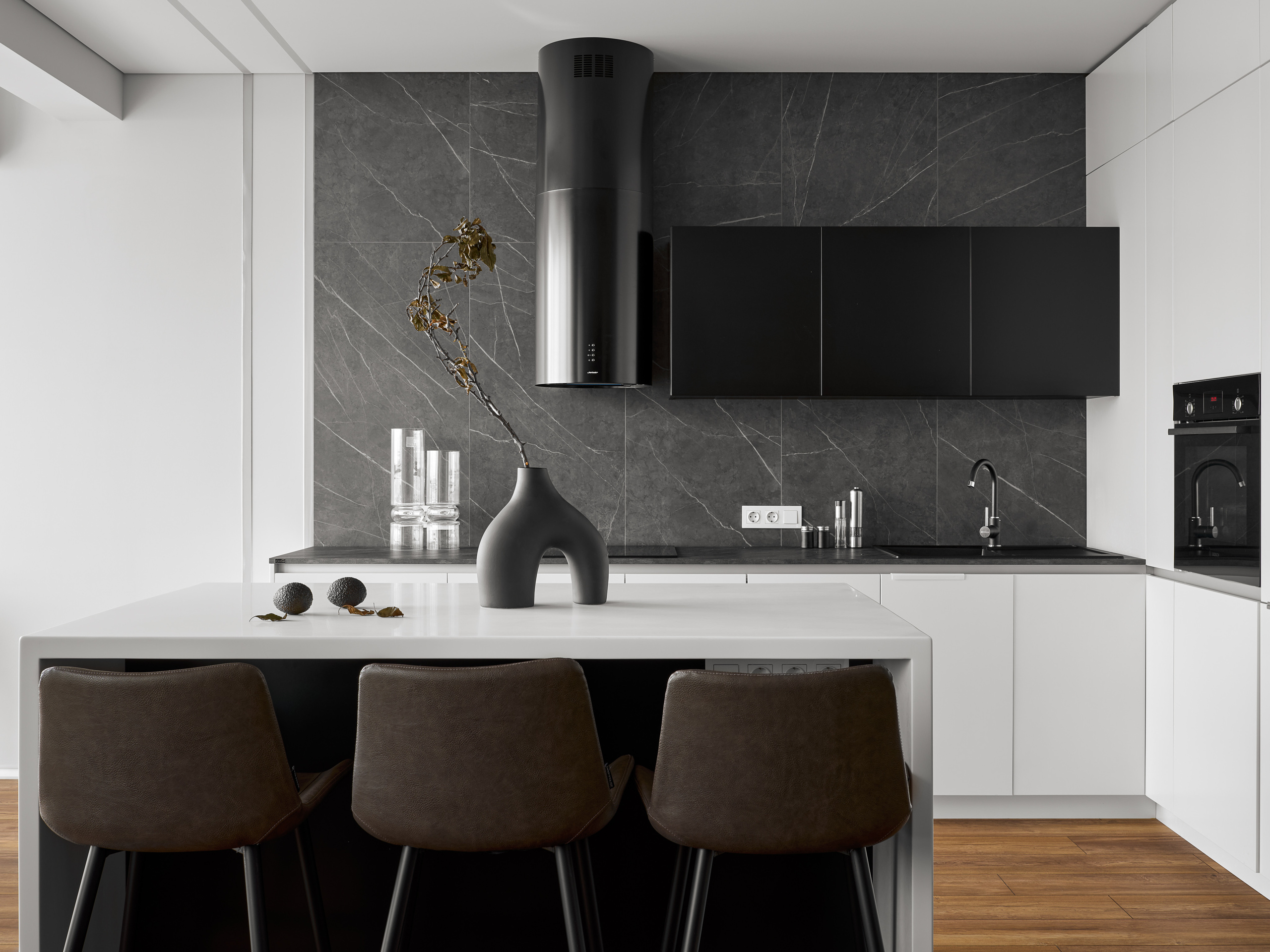 Современный кухонный остров с белой столешницей, дизайнерской вазой и барными стульями, серый каменный фартук в минимализме, авторский проект Андрея Неленя и Екатерины Проскуряковой, стилист Алина Нелень, фото Сергей Денисенко.
