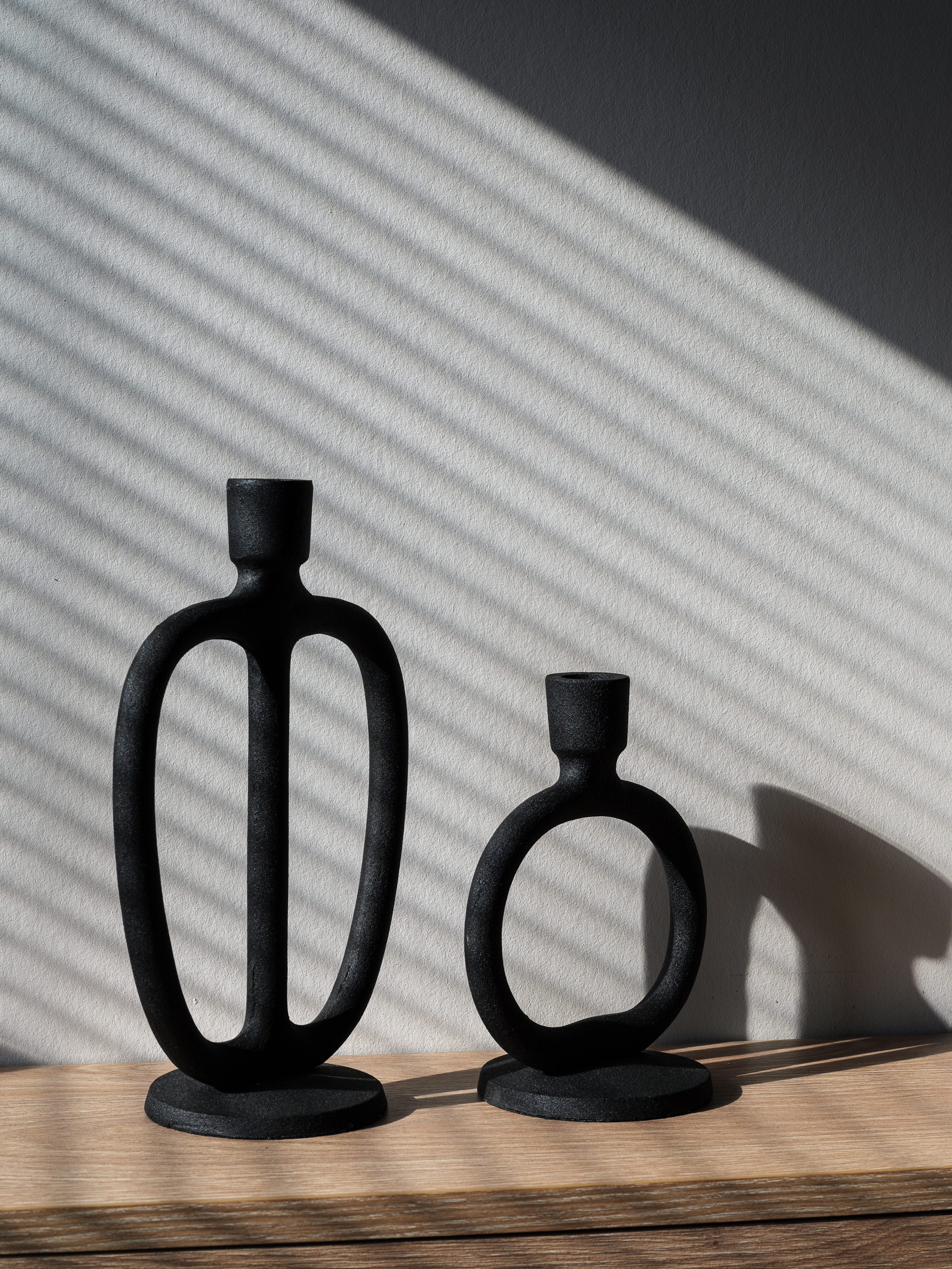 Декоративные чёрные подсвечники скульптурной формы на деревянной поверхности, акцент на игру света и тени от жалюзи, стильный минимализм в интерьере от Алёны Сверловой, фотограф Сергей Денисенко.