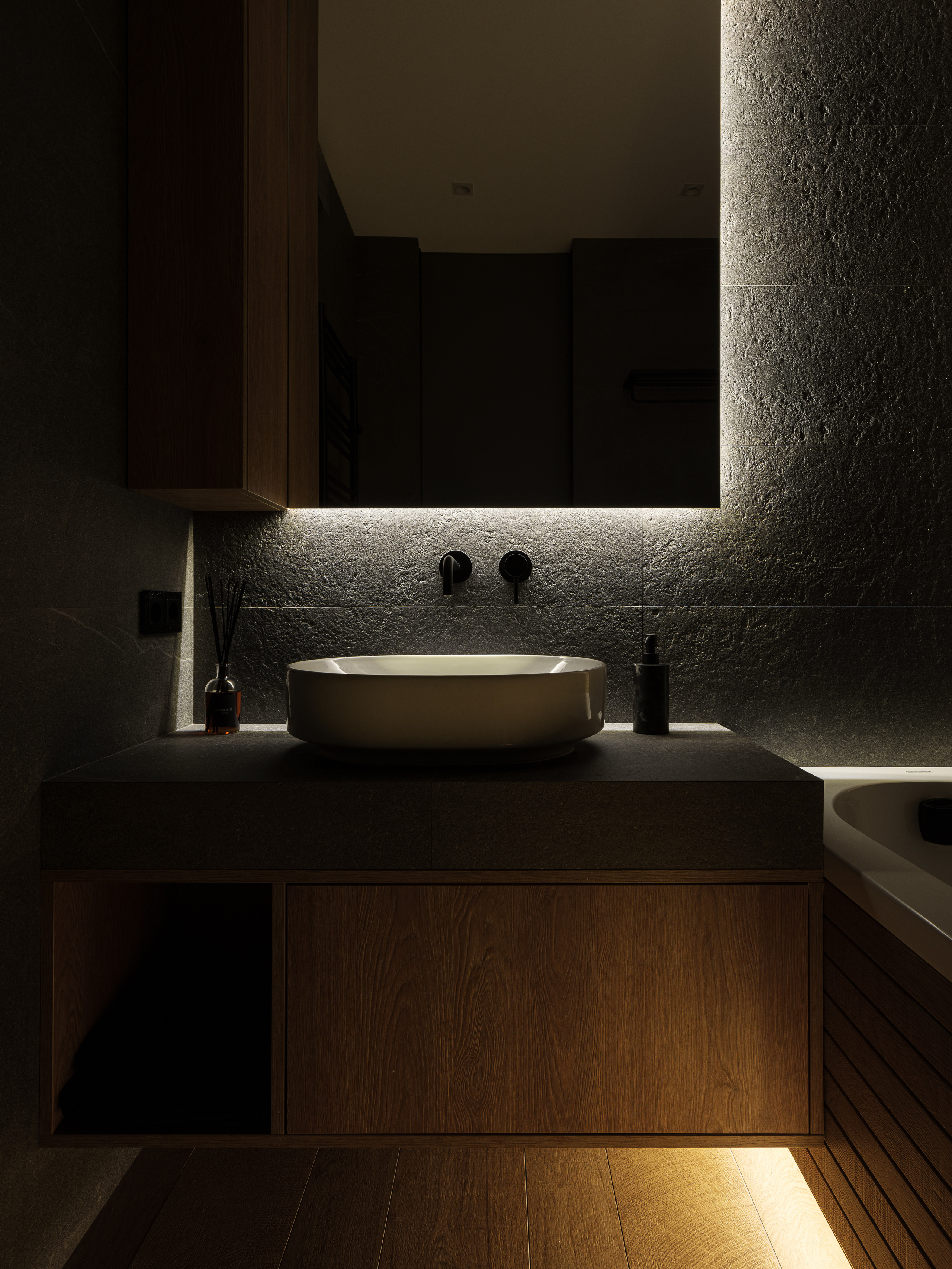 Современная ванная комната в минимализме с овальной раковиной на серой столешнице, деревянным шкафом, подсветкой под зеркалом и теплым светом под мебелью, гармоничный интерьер от дизайнера Алёны Сверловой, фото Сергея Денисенко.