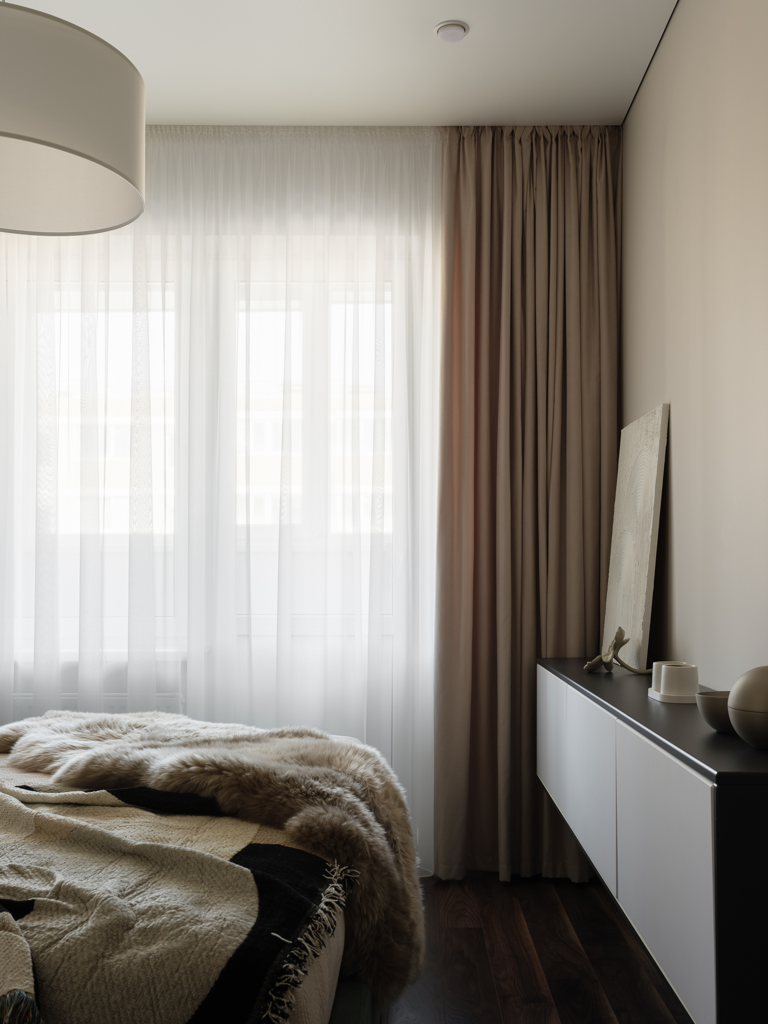 Современная спальня с большим окном, воздушными шторами, мягким пледом и минималистичной мебелью, сочетание текстиля и светлых тонов в интерьере от Алины Нелень, интерьерная фотосъёмка Сергея Денисенко.