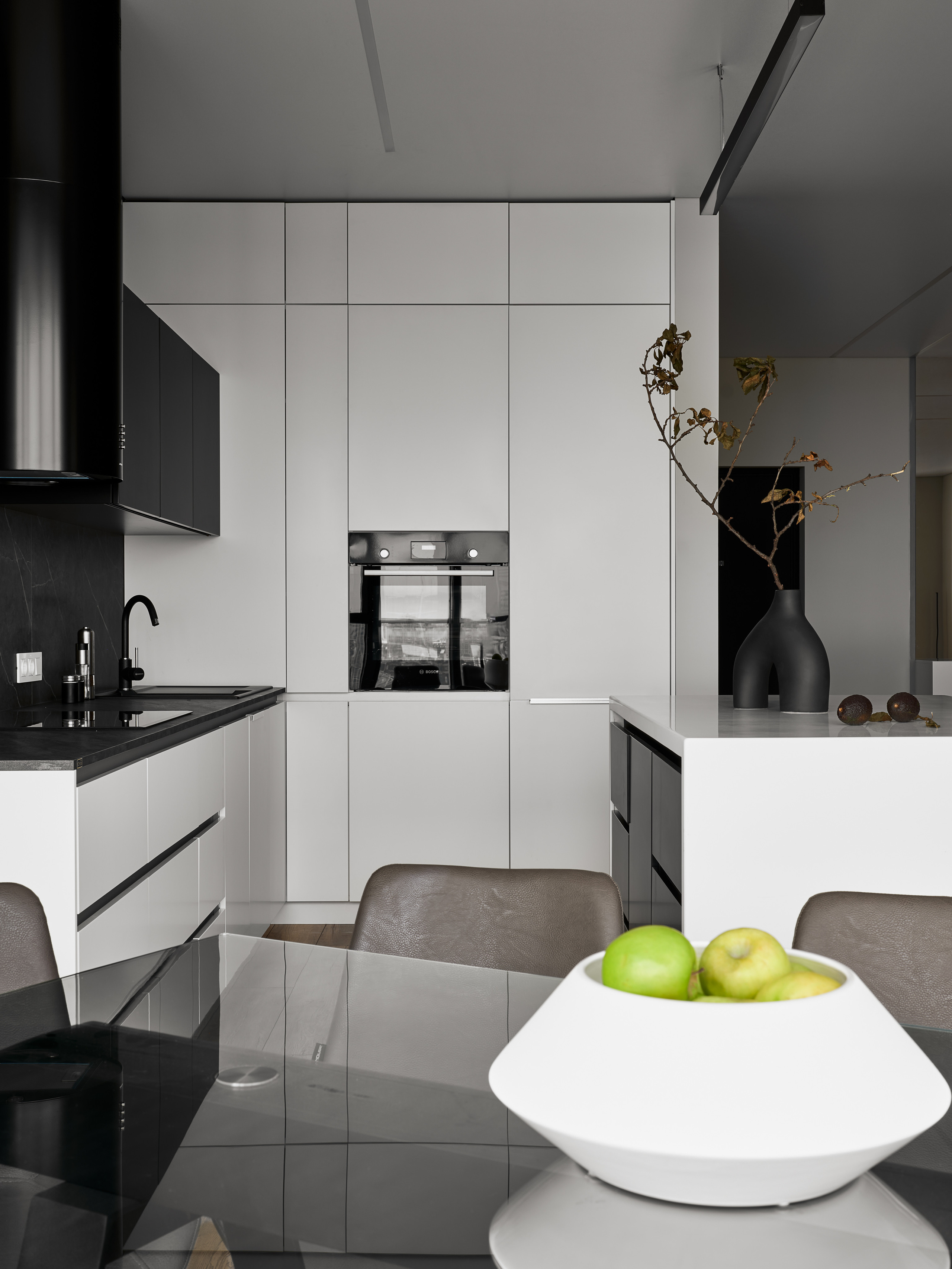 Интерьер кухни-столовой с белыми фасадами, встроенной техникой, акцентной вазой и обеденной зоной, проект Андрея Неленя и Екатерины Проскуряковой, визуальная стилистика Алины Нелень, фотография Сергея Денисенко.