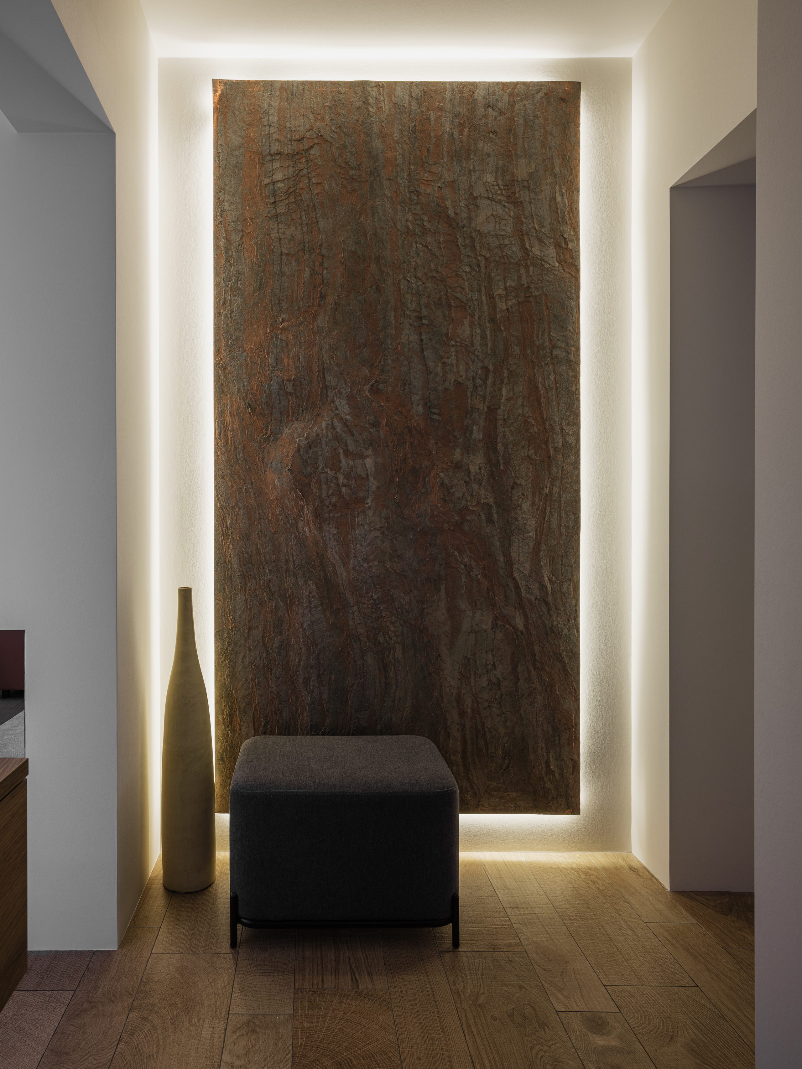Современный интерьер коридора с акцентной стеной из натурального камня с подсветкой, стильным пуфом и высокой декоративной вазой; минимализм и природные материалы. Дизайн Алёна Сверлова, фото Сергей Денисенко.