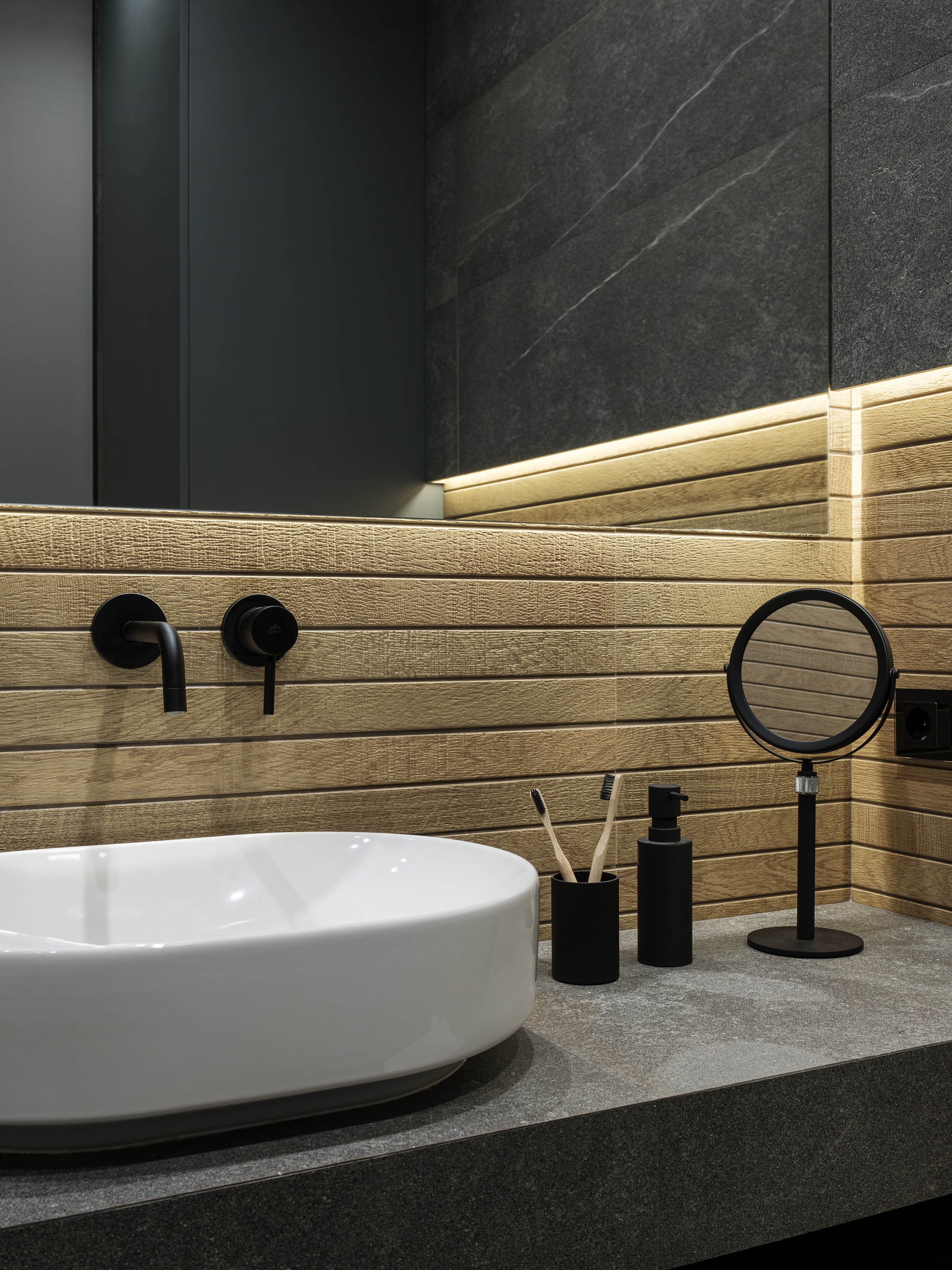 Стильная раковина на каменной столешнице в окружении деревянных панелей и серого керамогранита, черные аксессуары и зеркало с подсветкой, современный интерьер ванной комнаты от Алёны Сверловой, фото Сергей Денисенко.