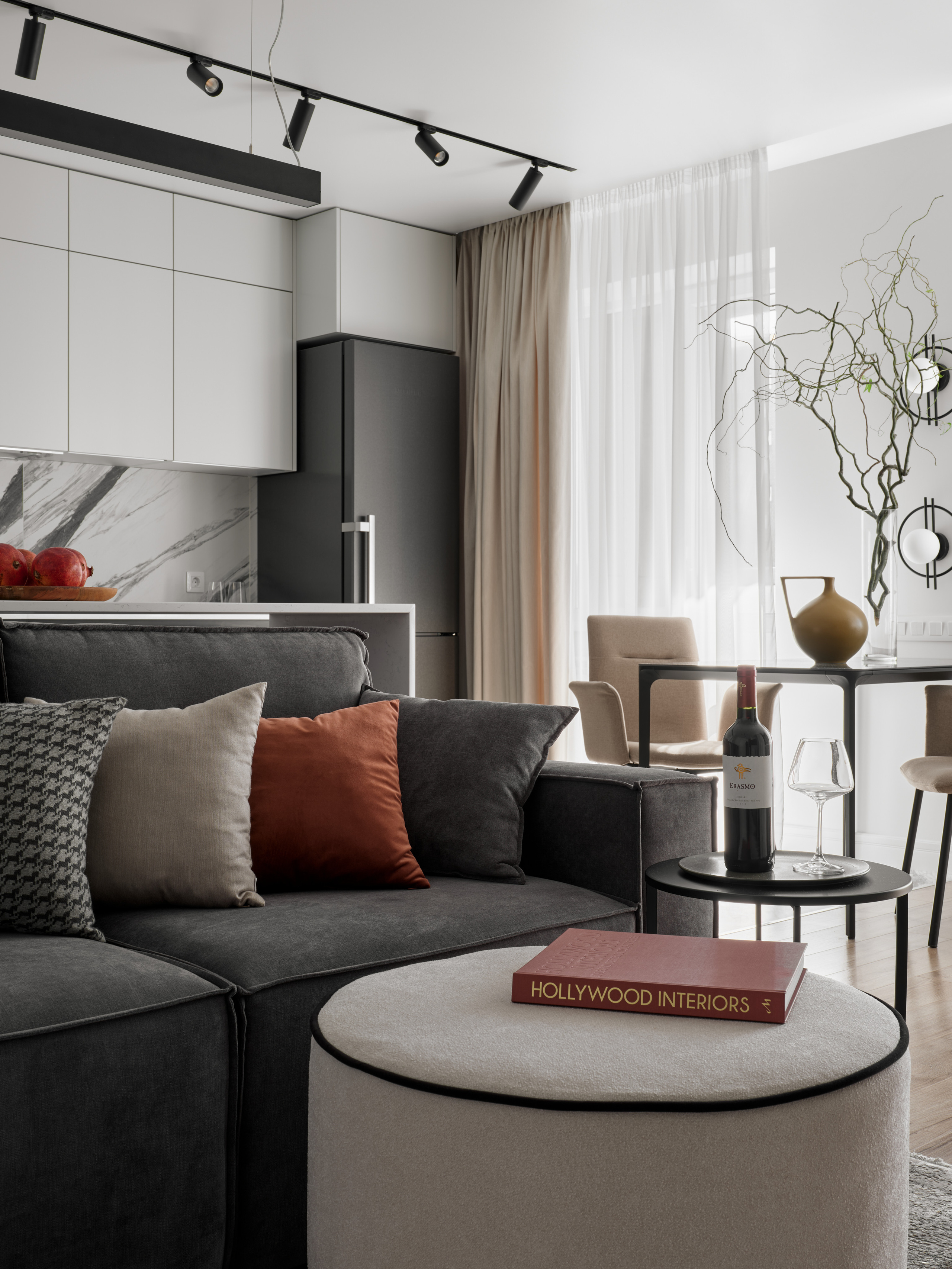 Современная гостиная с серым диваном, акцентными подушками, журнальным столиком и кухней с мраморным фартуком на фоне. Интерьер от Екатерины Мищенко, автор фото – Сергей Денисенко.