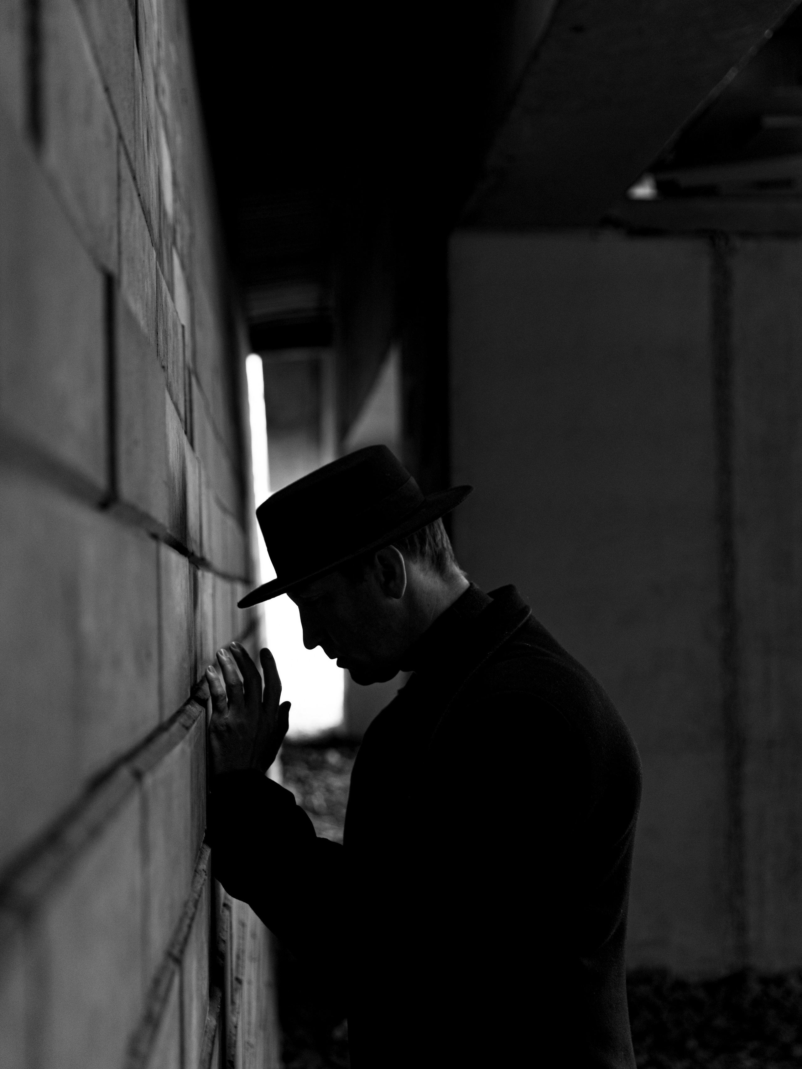 Черно-белый портрет мужчины в шляпе у стены