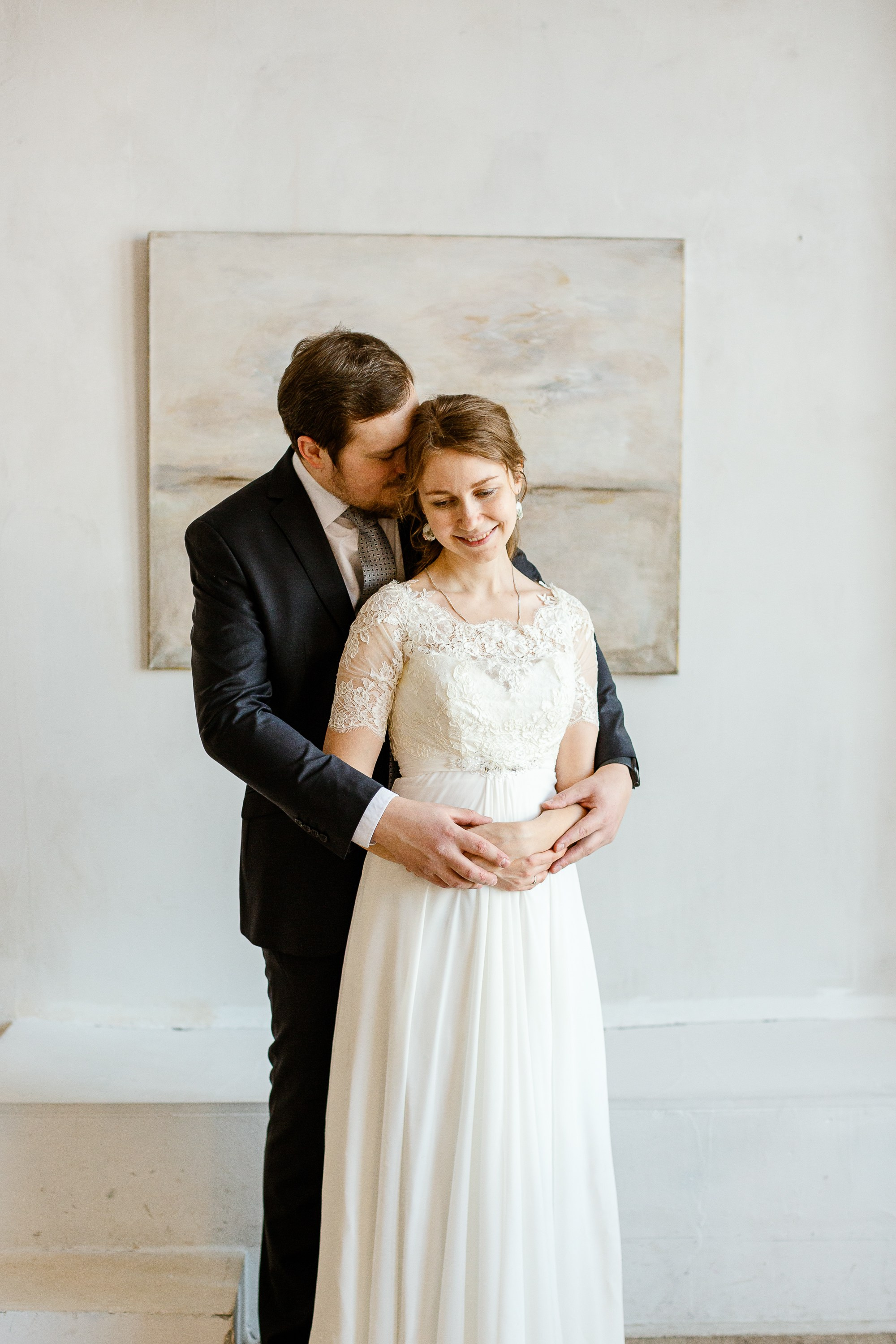 Жених и невеста в праздничной фотостудии. Жених в костюме, невеста в красивом белом платье. На фоне картина.