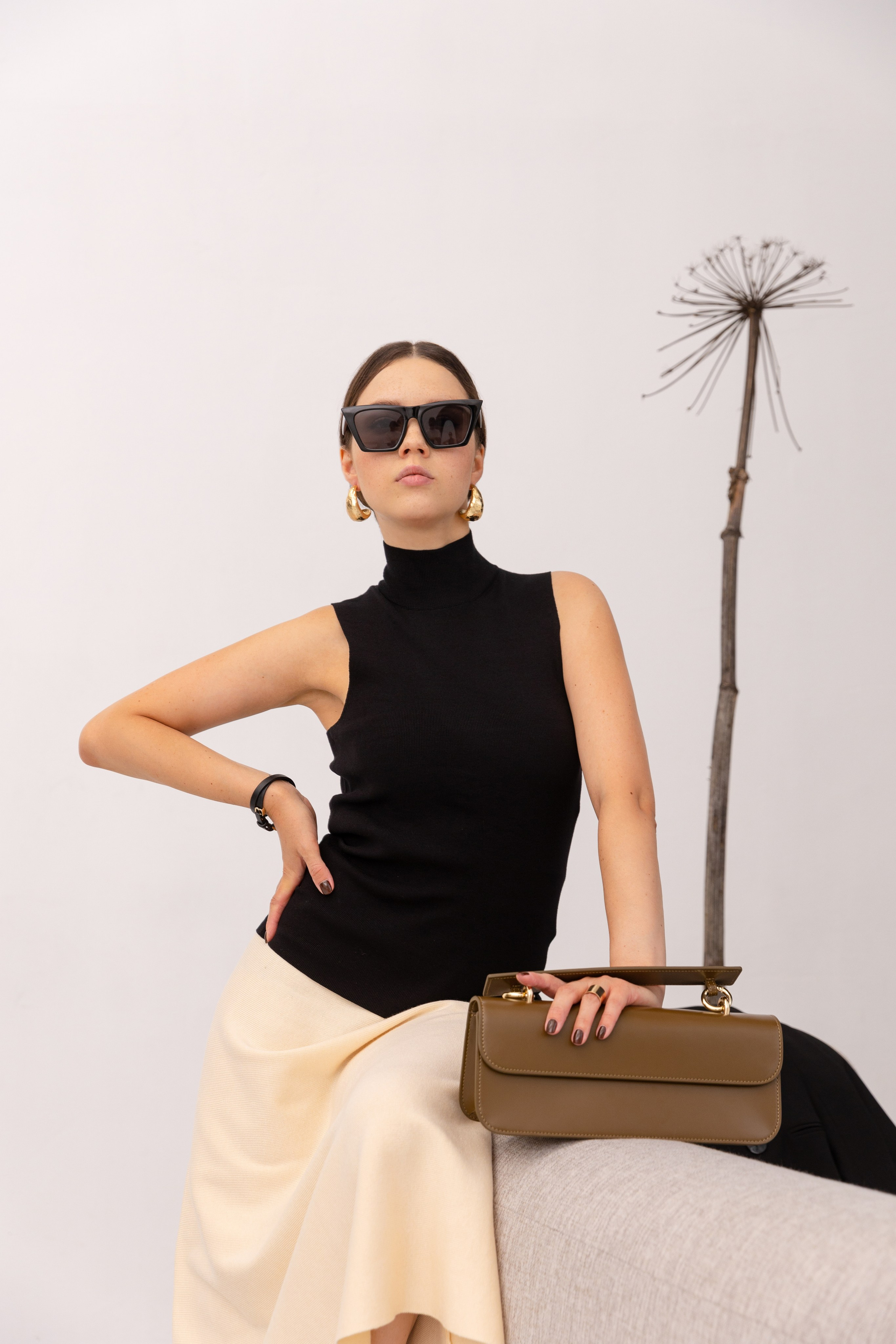 Девушка в стильным модным образе сидит на диване сзади кустик сухого борщевика