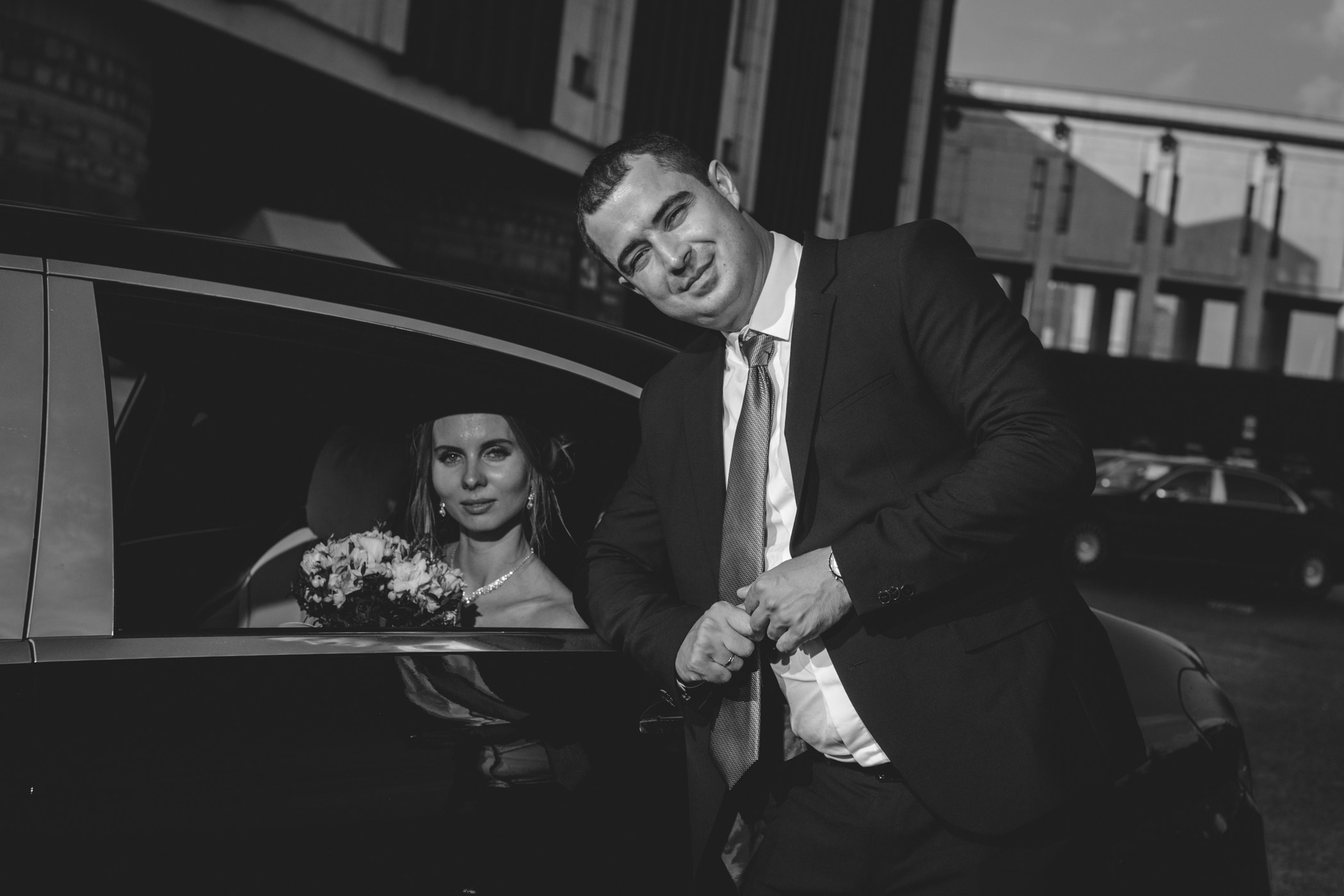 черно белое свадебное фото где невеста сидит в машине и рядом с ней стоит жених 