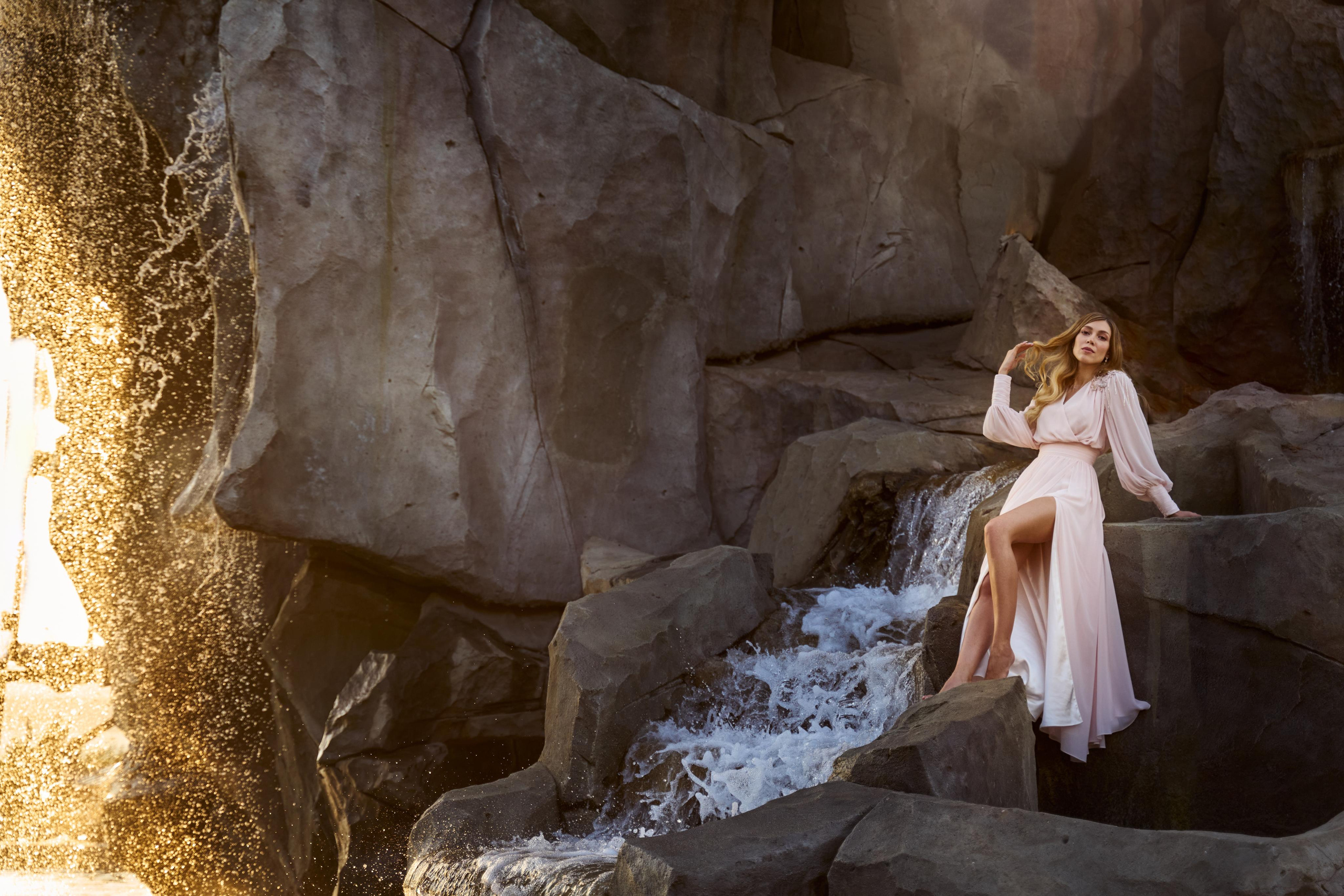 Невеста в белом платье у подножия скальной породы с водопадом, отражающей волшебную атмосферу замка Гарибальди.