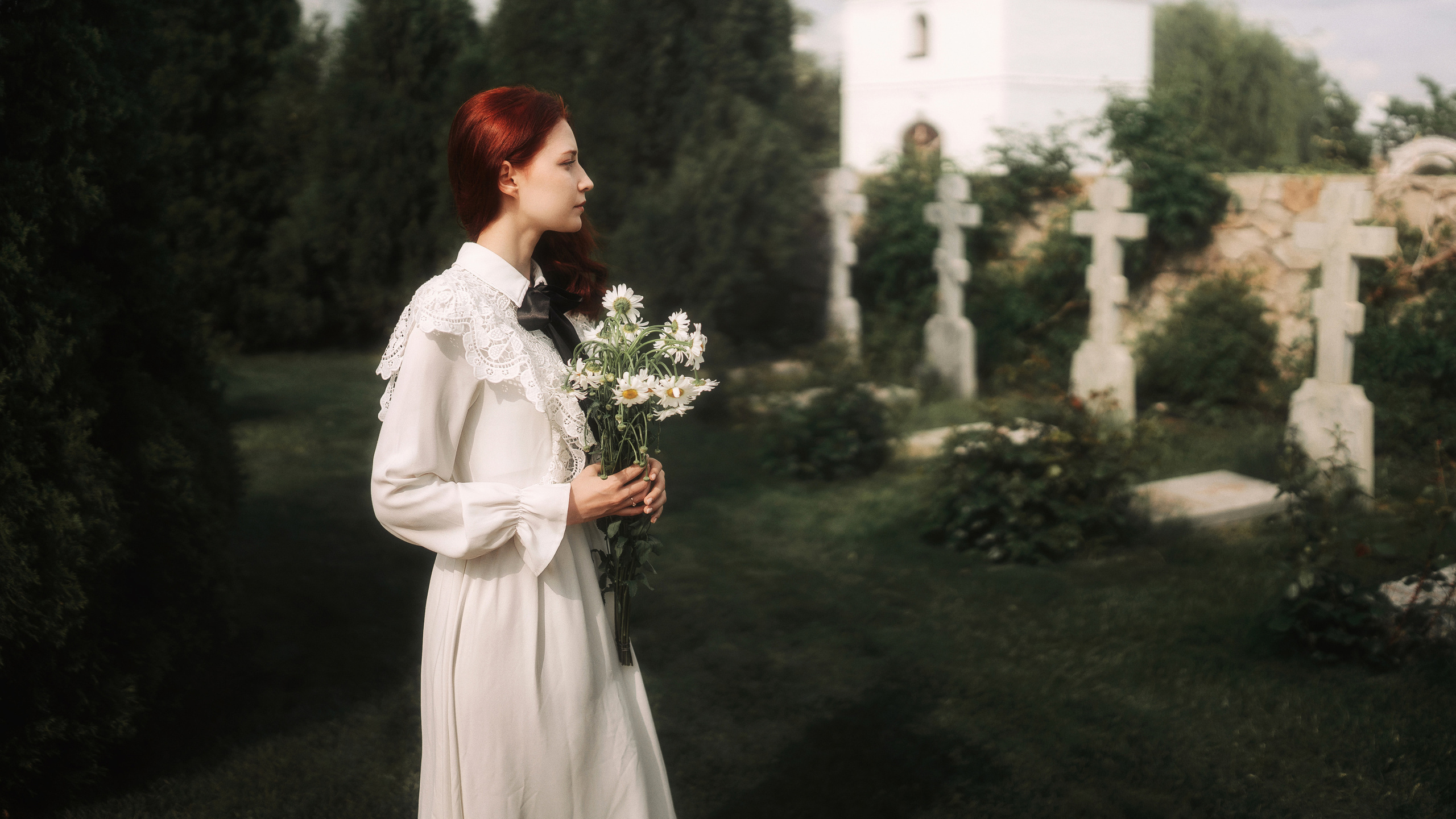 Рыжая девушка стоит около могильных захоронений.