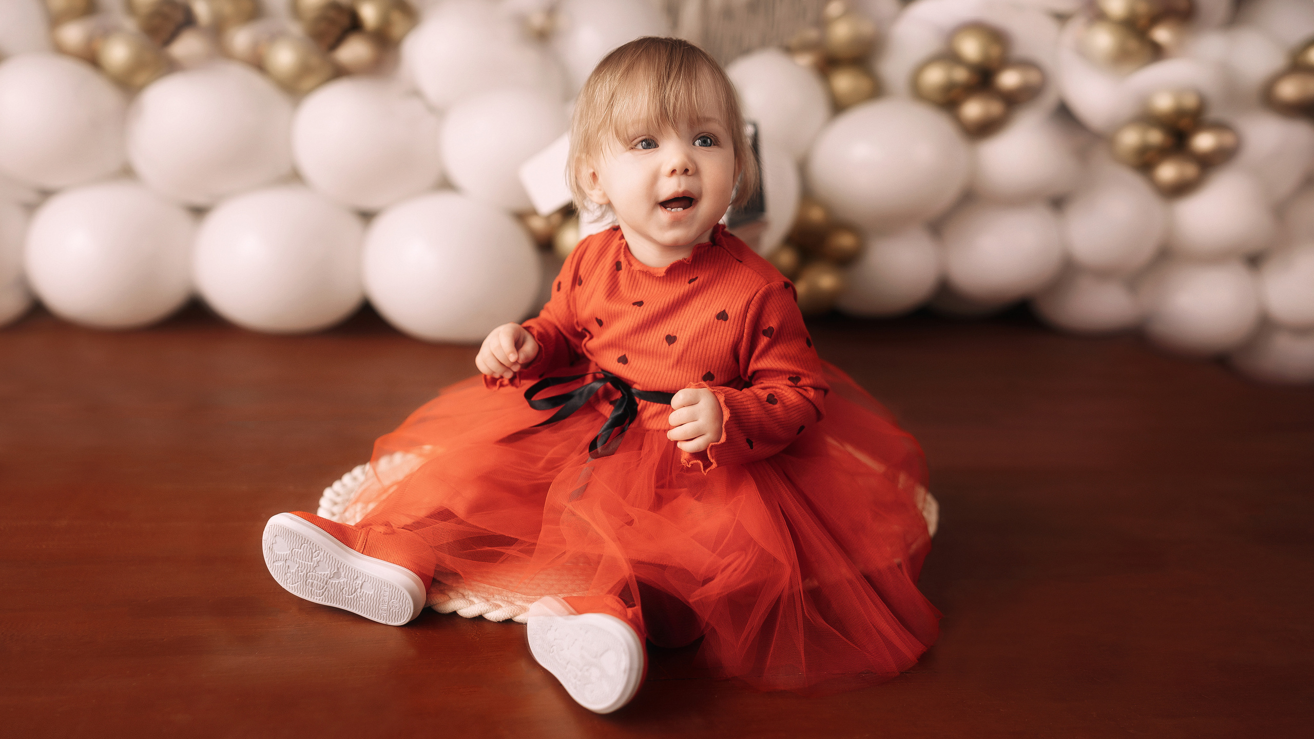 Девочка в красном платье улыбается, а на фоне красивые белые шарики.