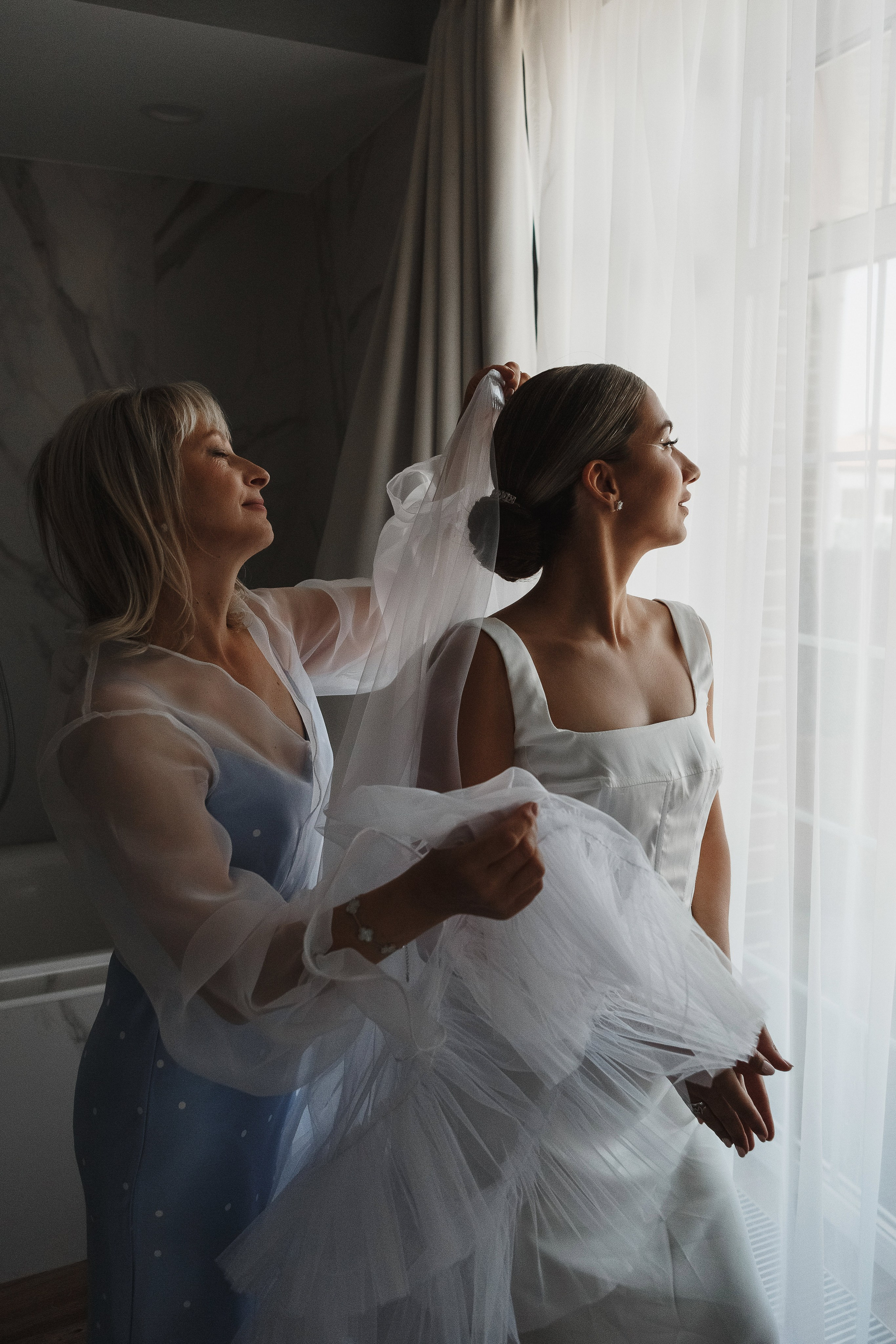 Мама помогает невесте надеть фату у окна в день свадьбы в комплексе Golden Horse, фотограф Таганрог Антон Бакарюк