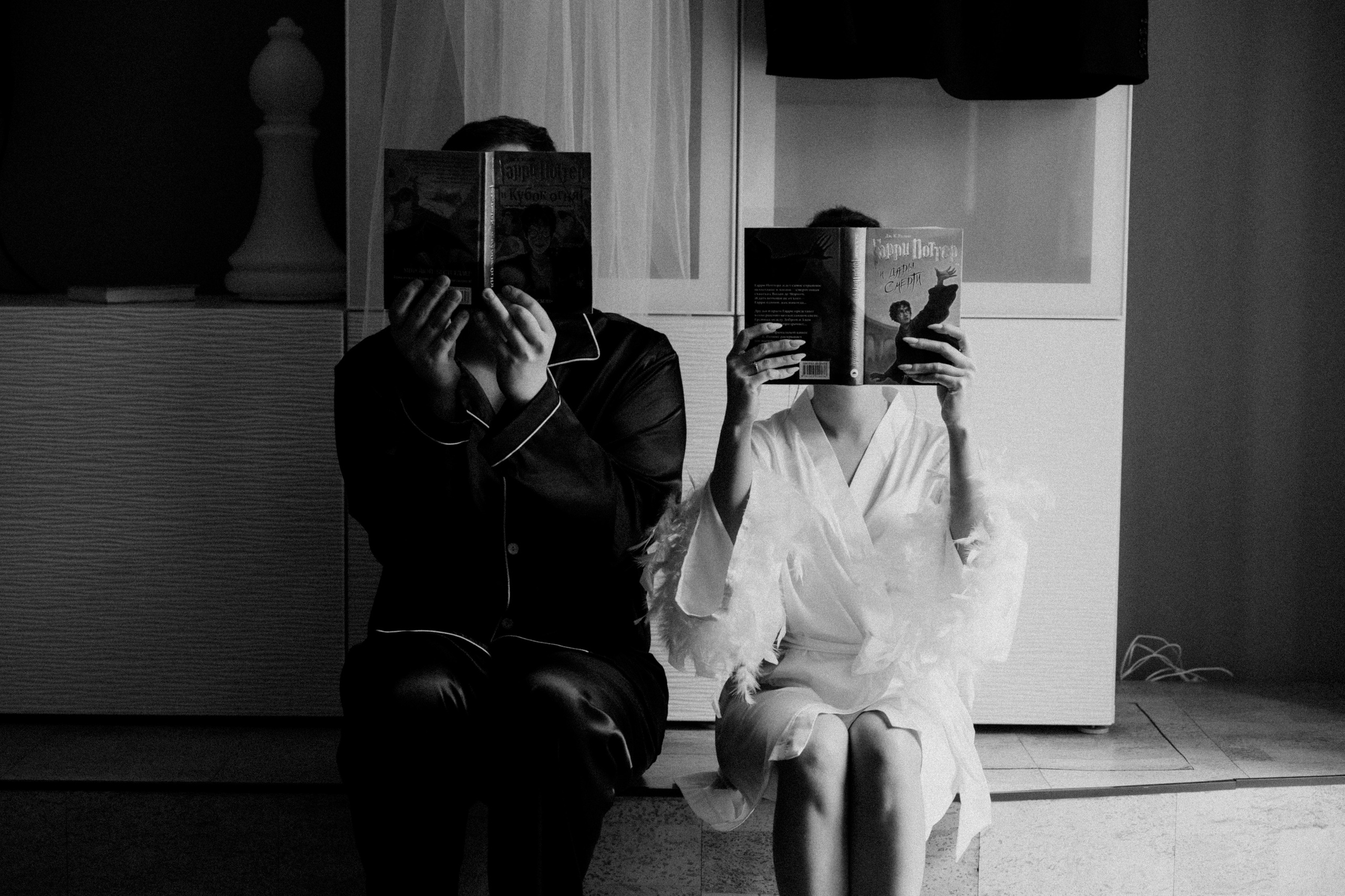 Жених и невеста сидят, закрыв лица книгами. Креативная и забавная свадебная фотосессия.