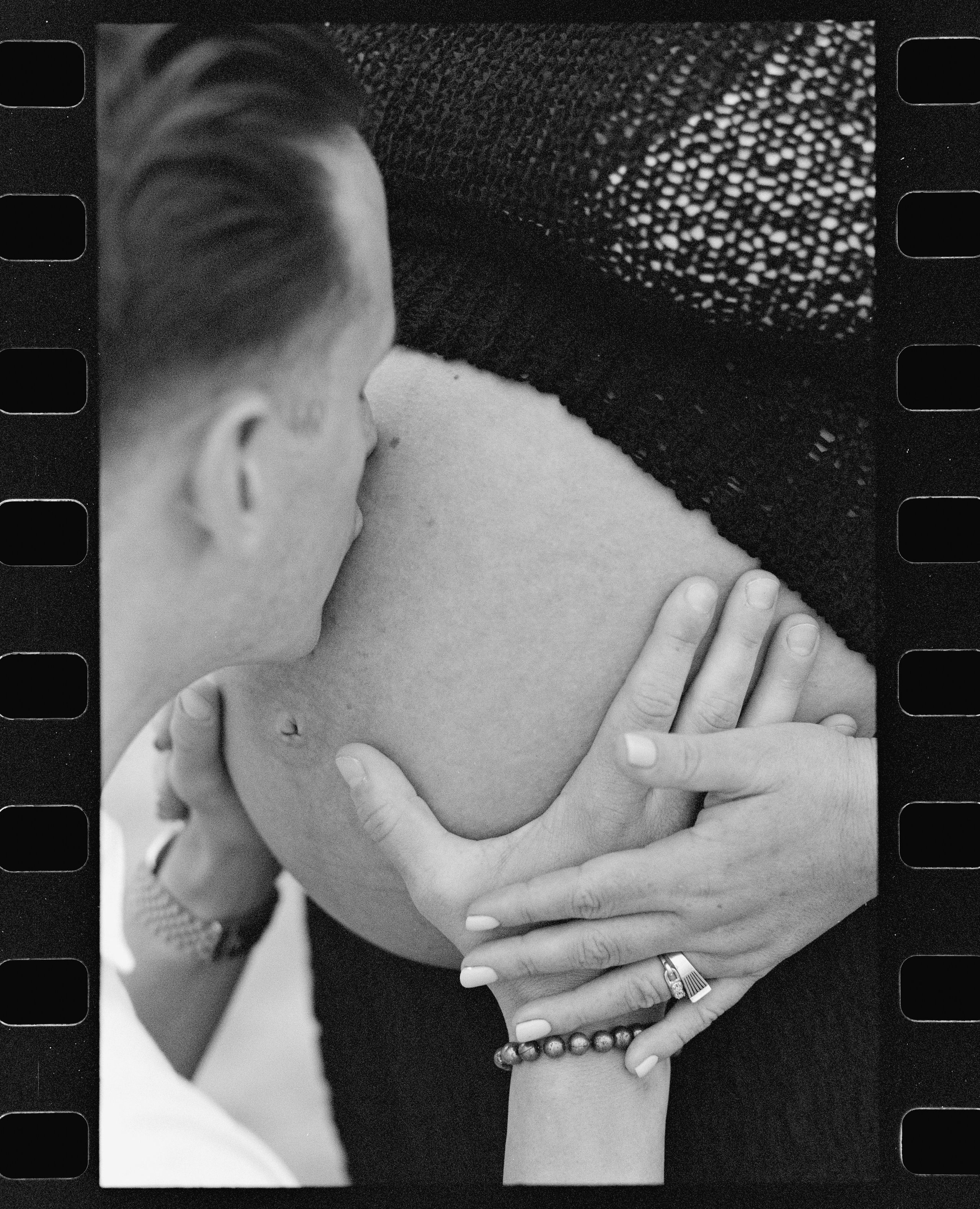 a black and white photo of a husband kissing wife's pregnant belly