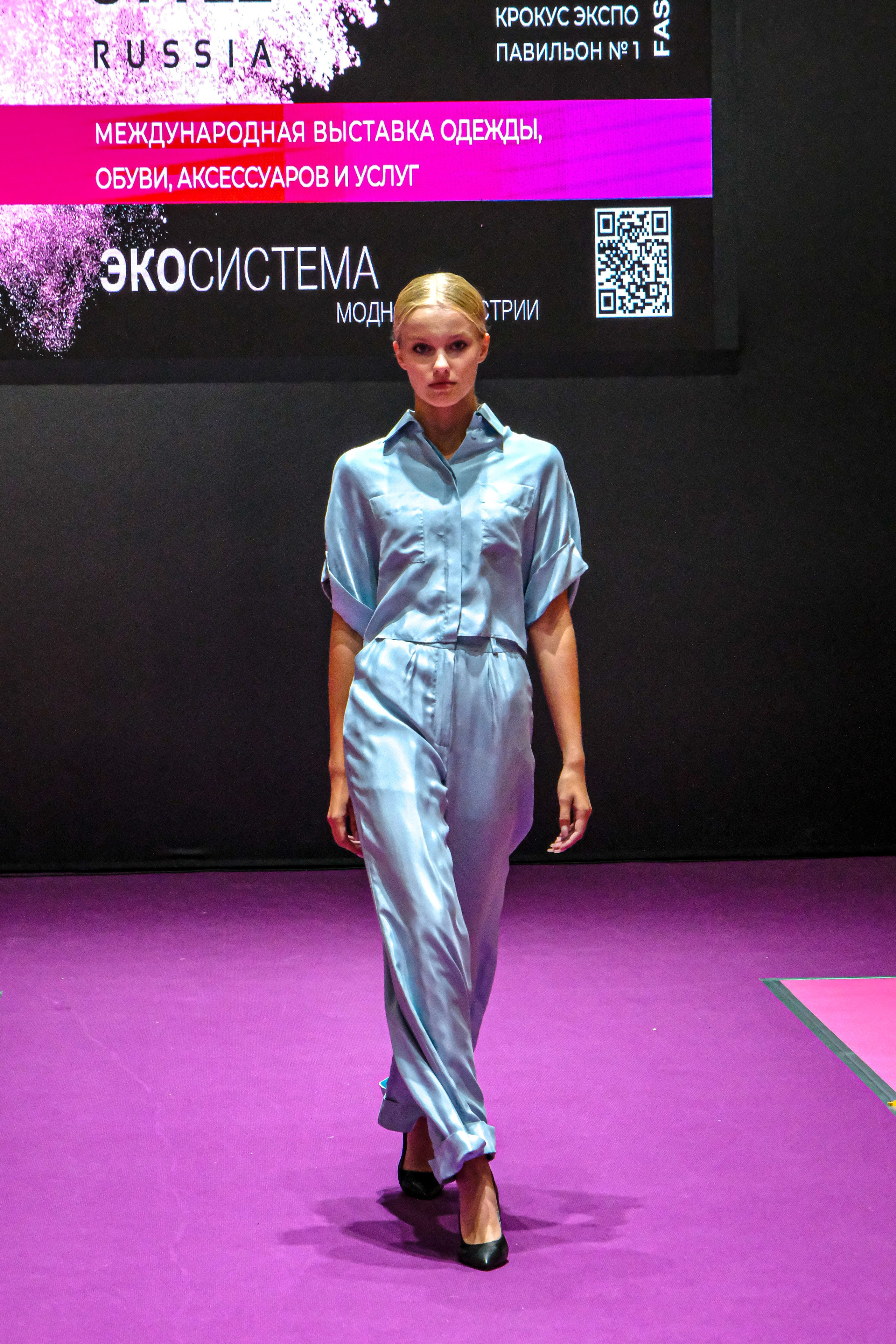  "Модели в ярких нарядах проходят по подиуму во время показа мод, освещенные яркими софитами и окруженные восторженными зрителями."