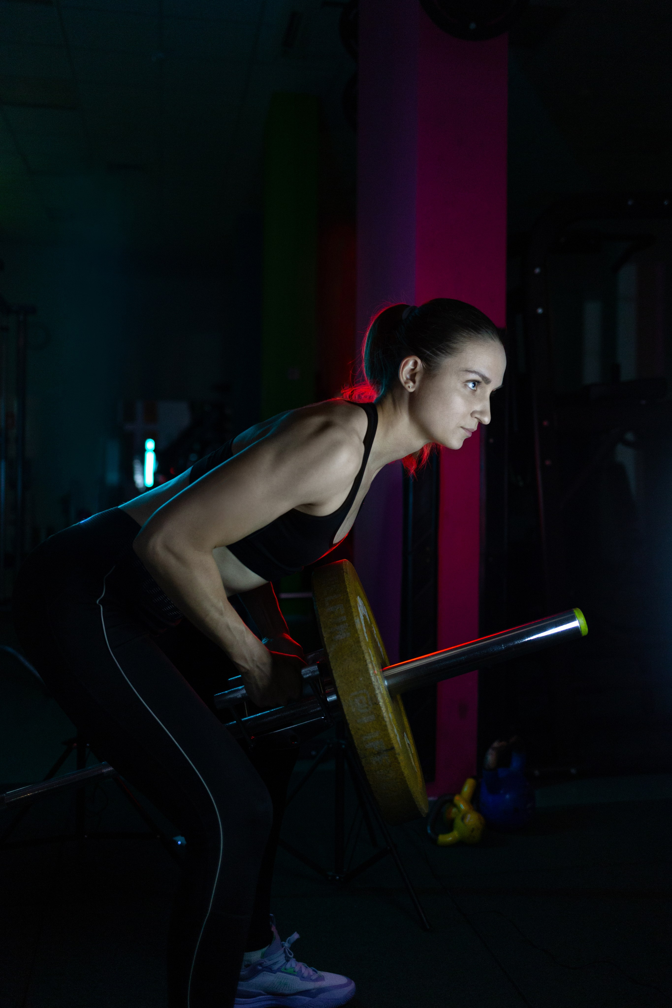 Девушка занимается со штангой. Работа со штангой в приседе. Темное спортивное стильное фото.