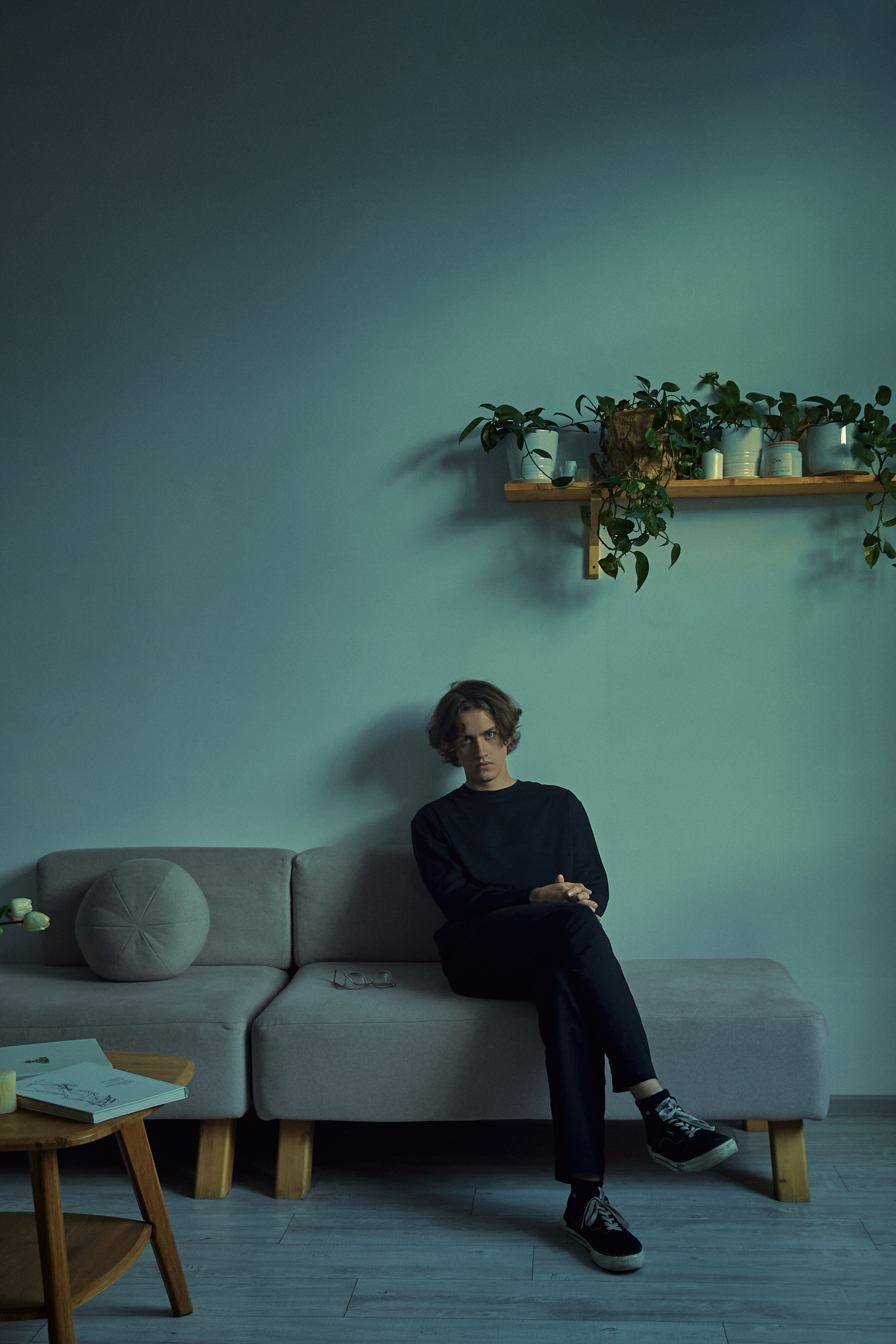 Парень на диване в синем свете на фоне белой стены