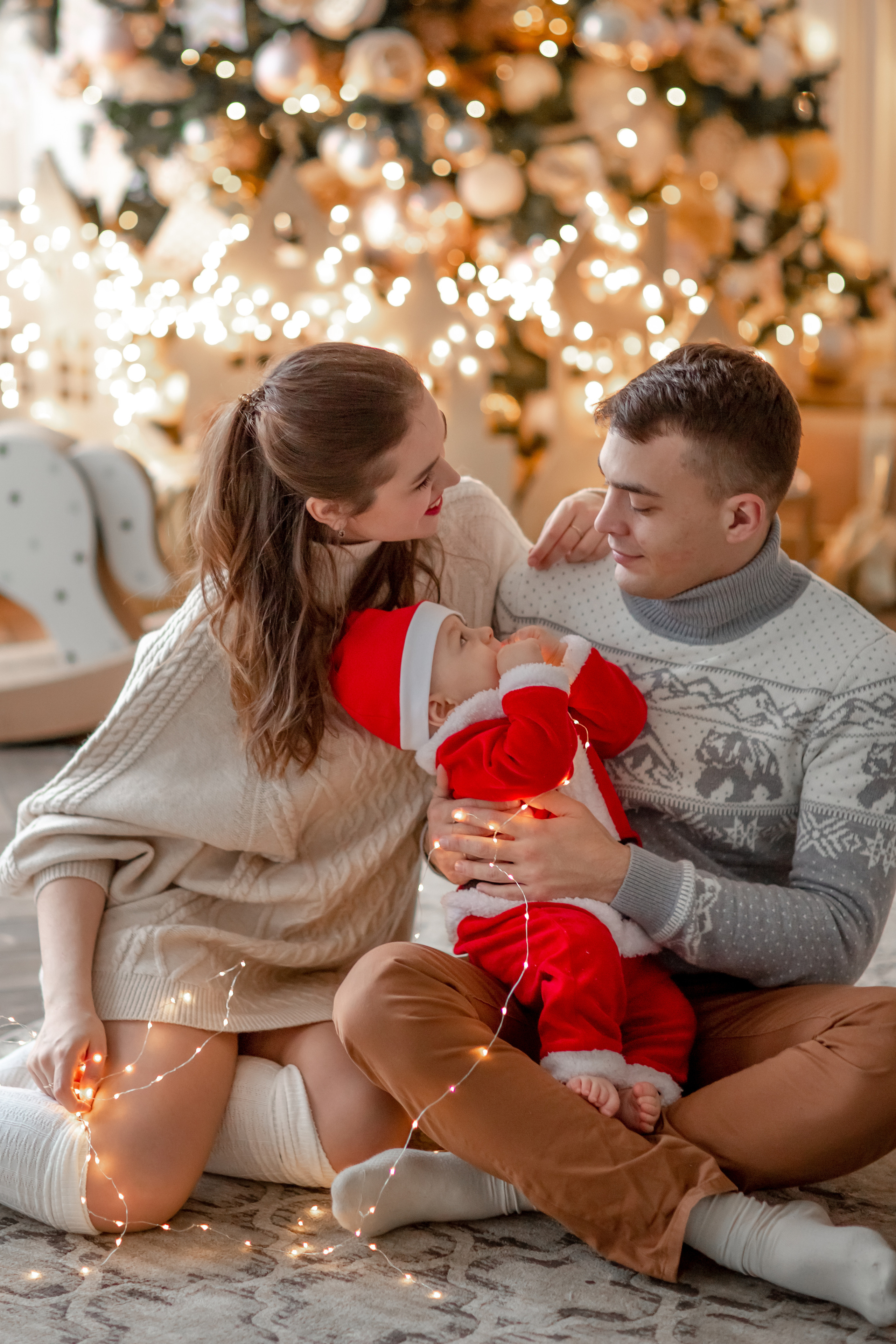 девушка, парень и ребёнок смотрят друг на друга на фоне новогодней ёлки