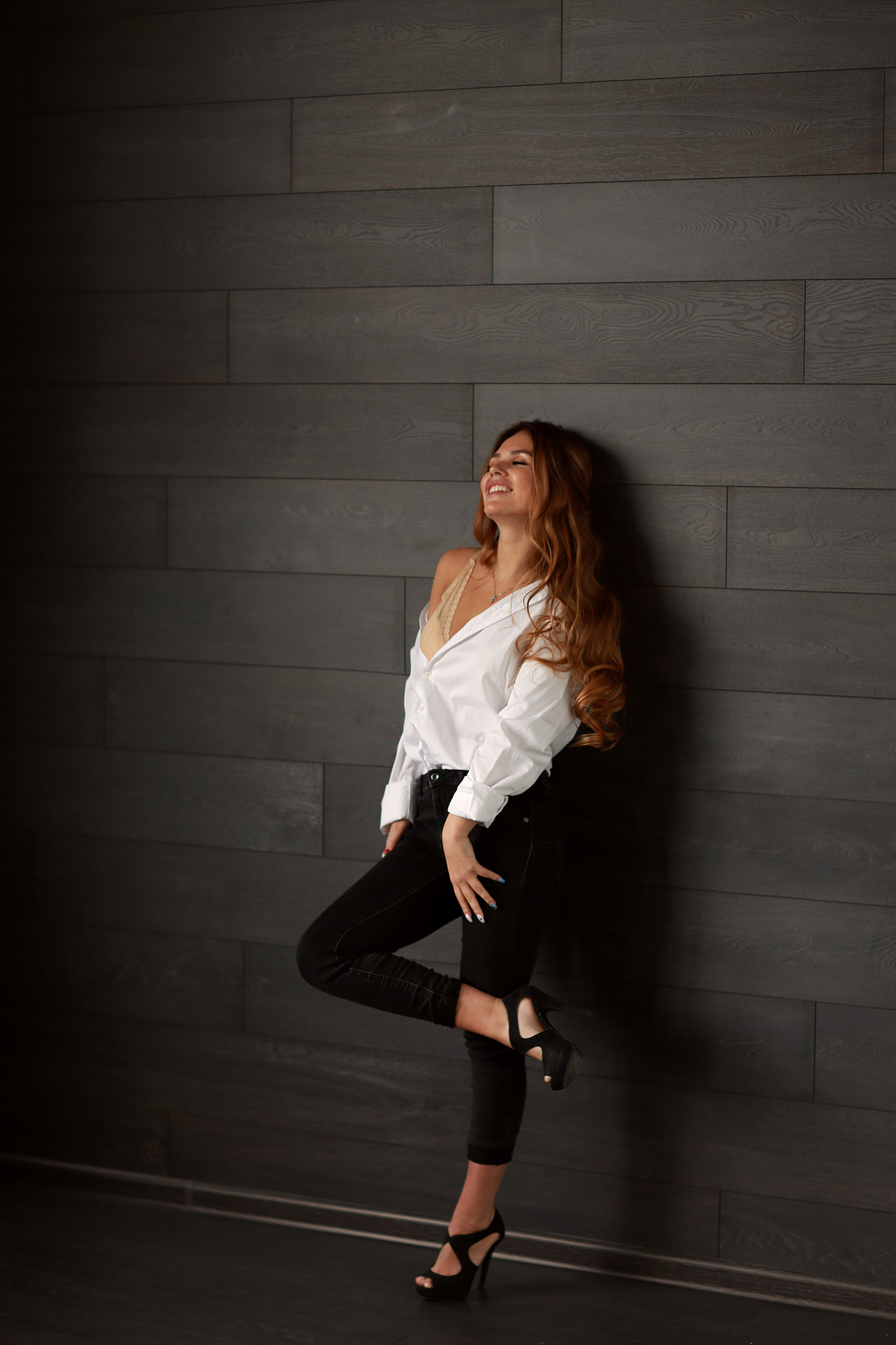 девушка в белой рубашке и черных штанах стоит на фоне графитовой стены