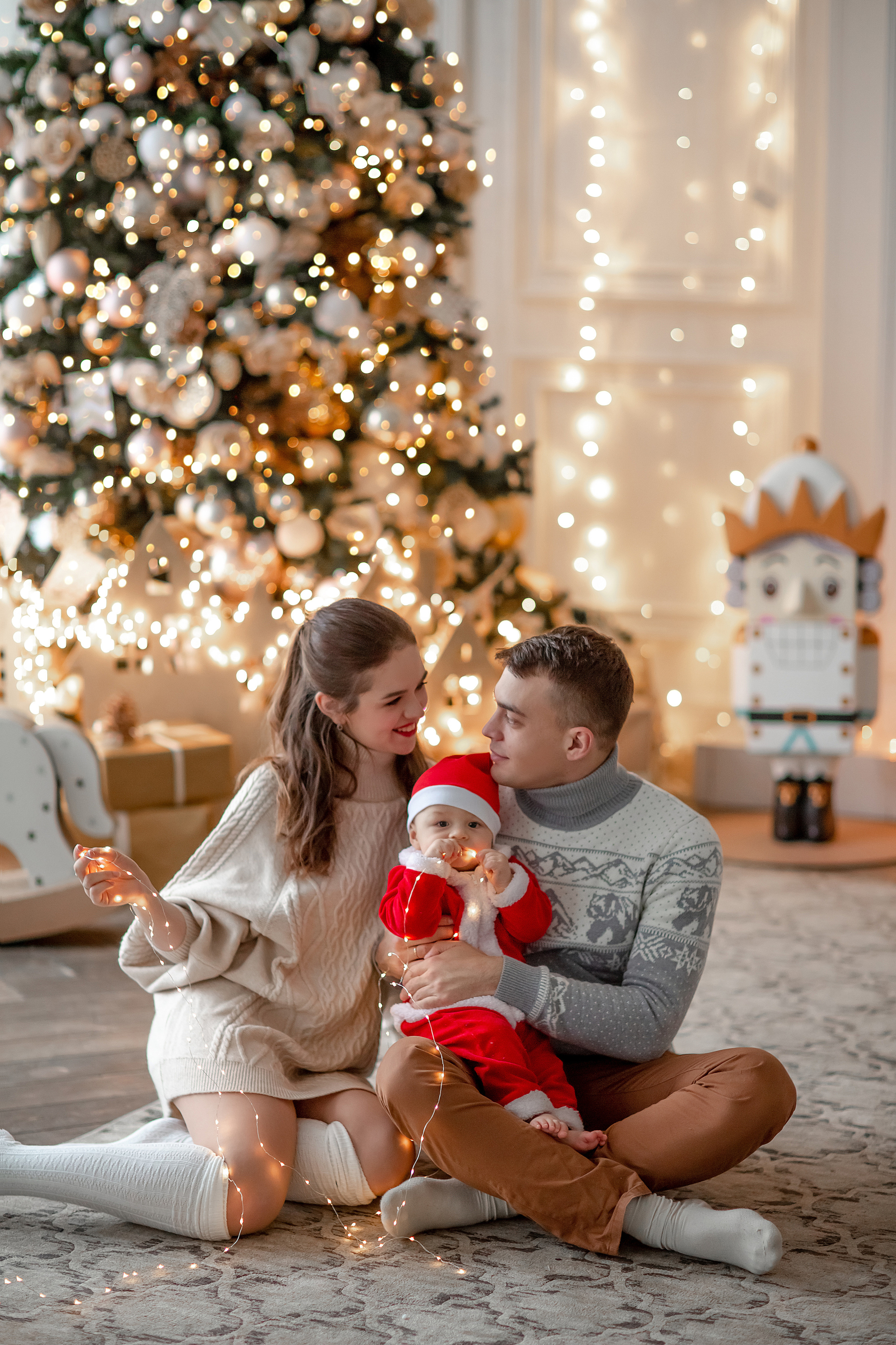 мама, папа и сын сидят на полу около новогодней ёлки