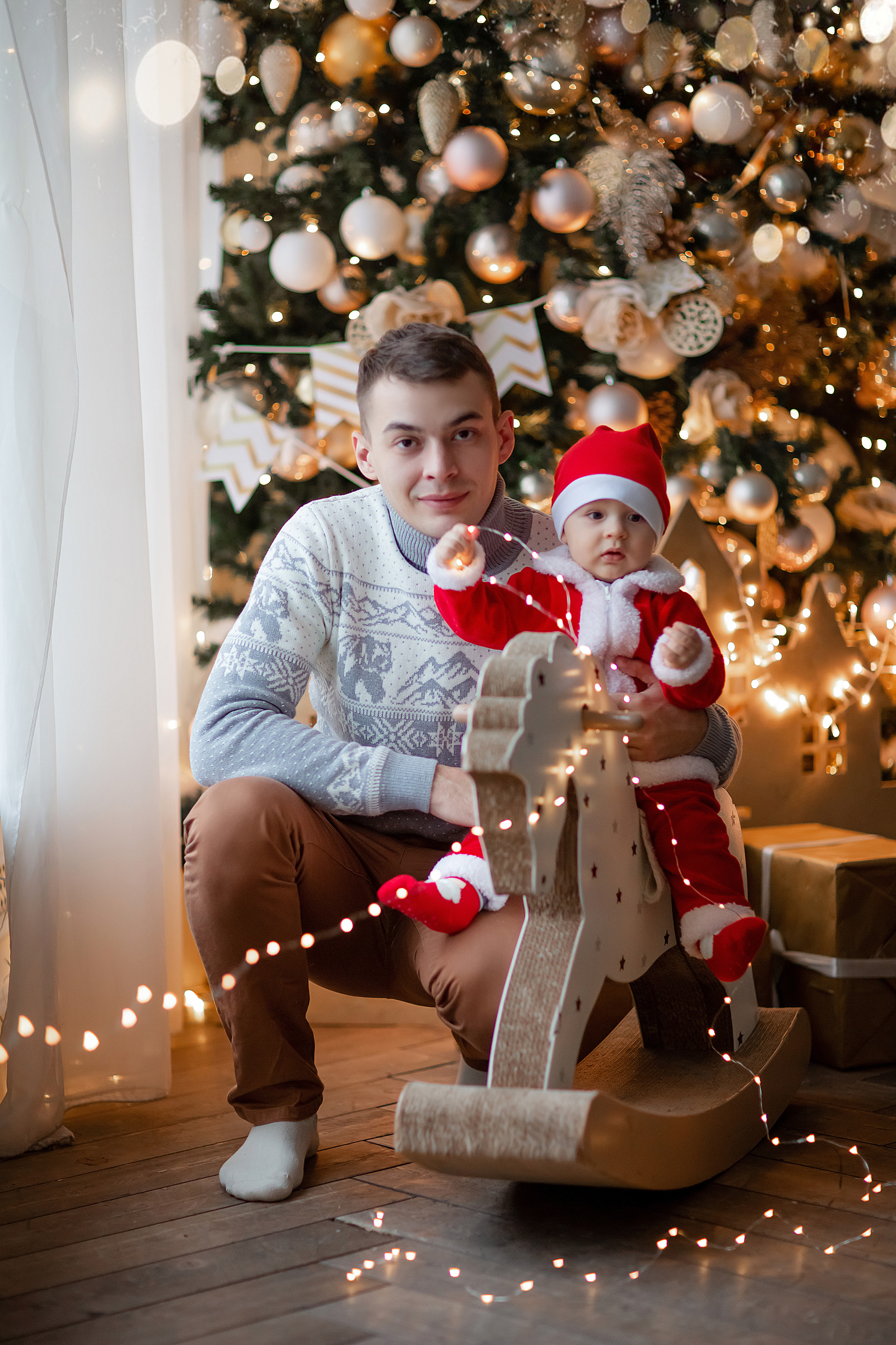папа и сын в новогодней фотостудии, сын сидит на деревянной лошадке