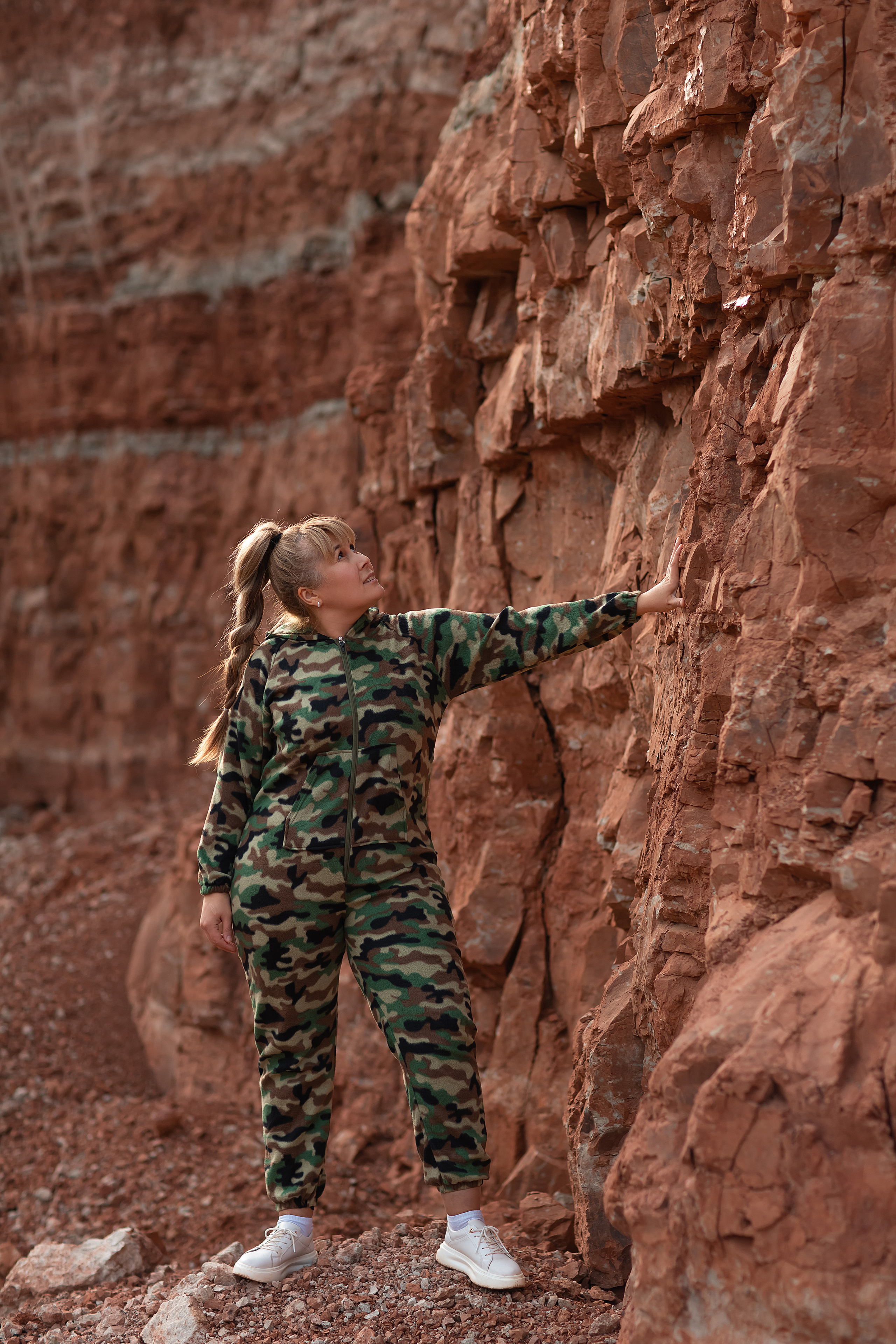 девушка в зелёном защитного цвета комбинезоне стоит на карьере боком