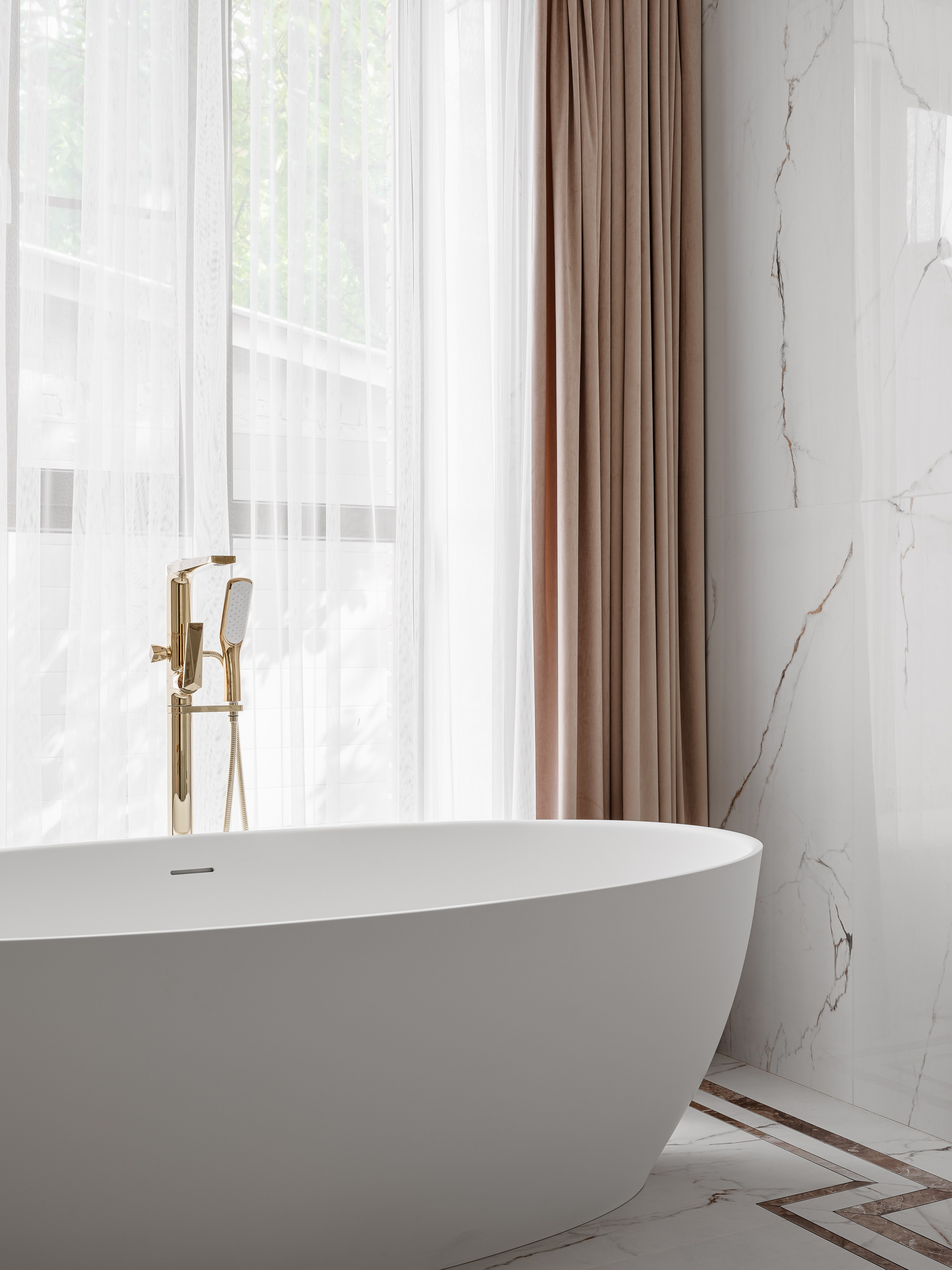 Изящная овальная белая ванна у панорамного окна с бежевыми шторами и золотым смесителем в интерьере ванной комнаты. Дизайнер Евгения Ермошина, фото Сергея Денисенко.