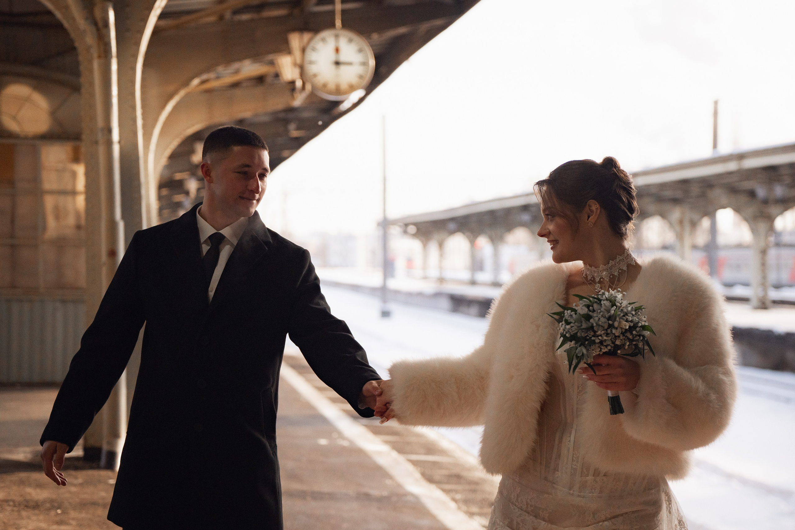 Свадебная фотосессия на Витебском вокзале в Санкт-Петербурге фото невесты и жениха. Держатся за руки и идут по перрону в лучах закатного солнца