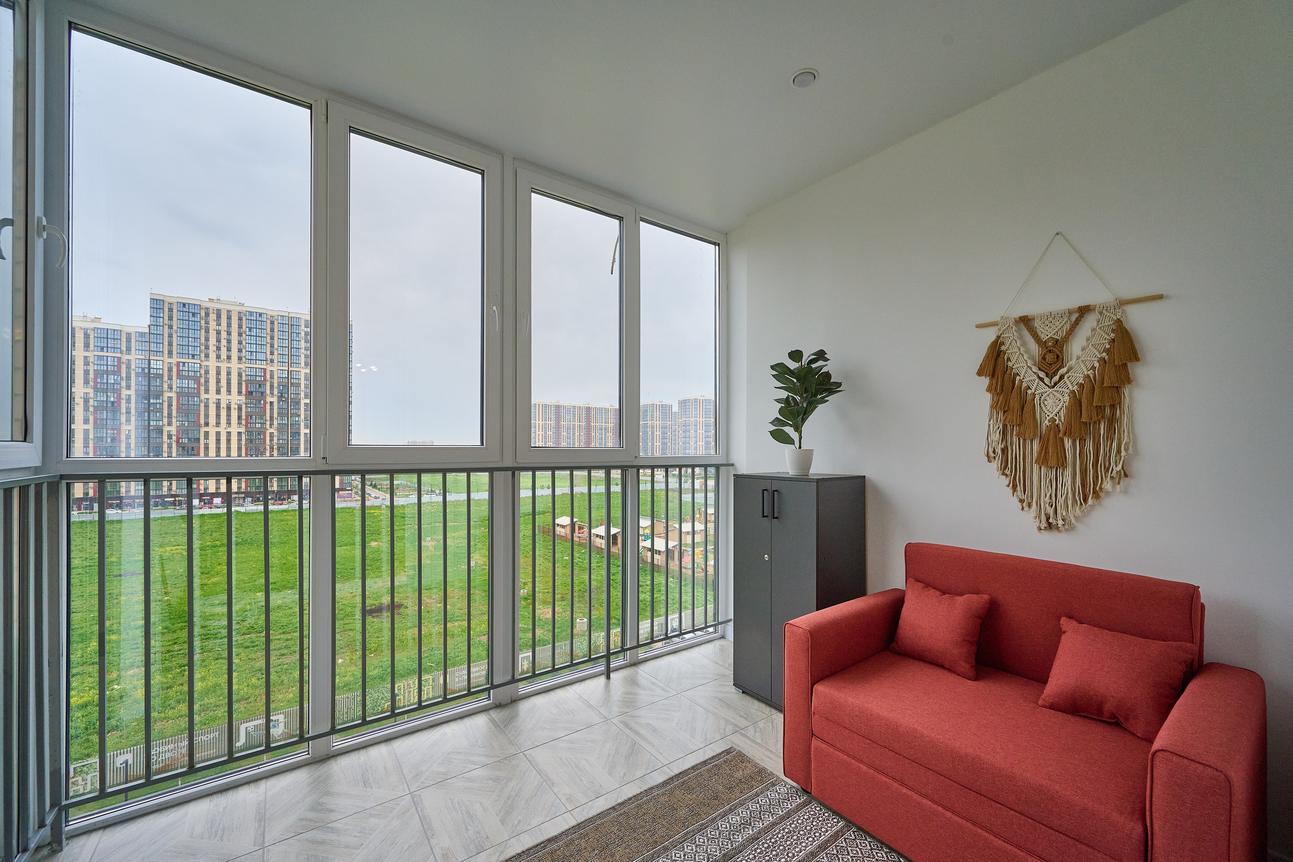 огромный балкон панорамные окна до пола красный диван серая тумбочка 
