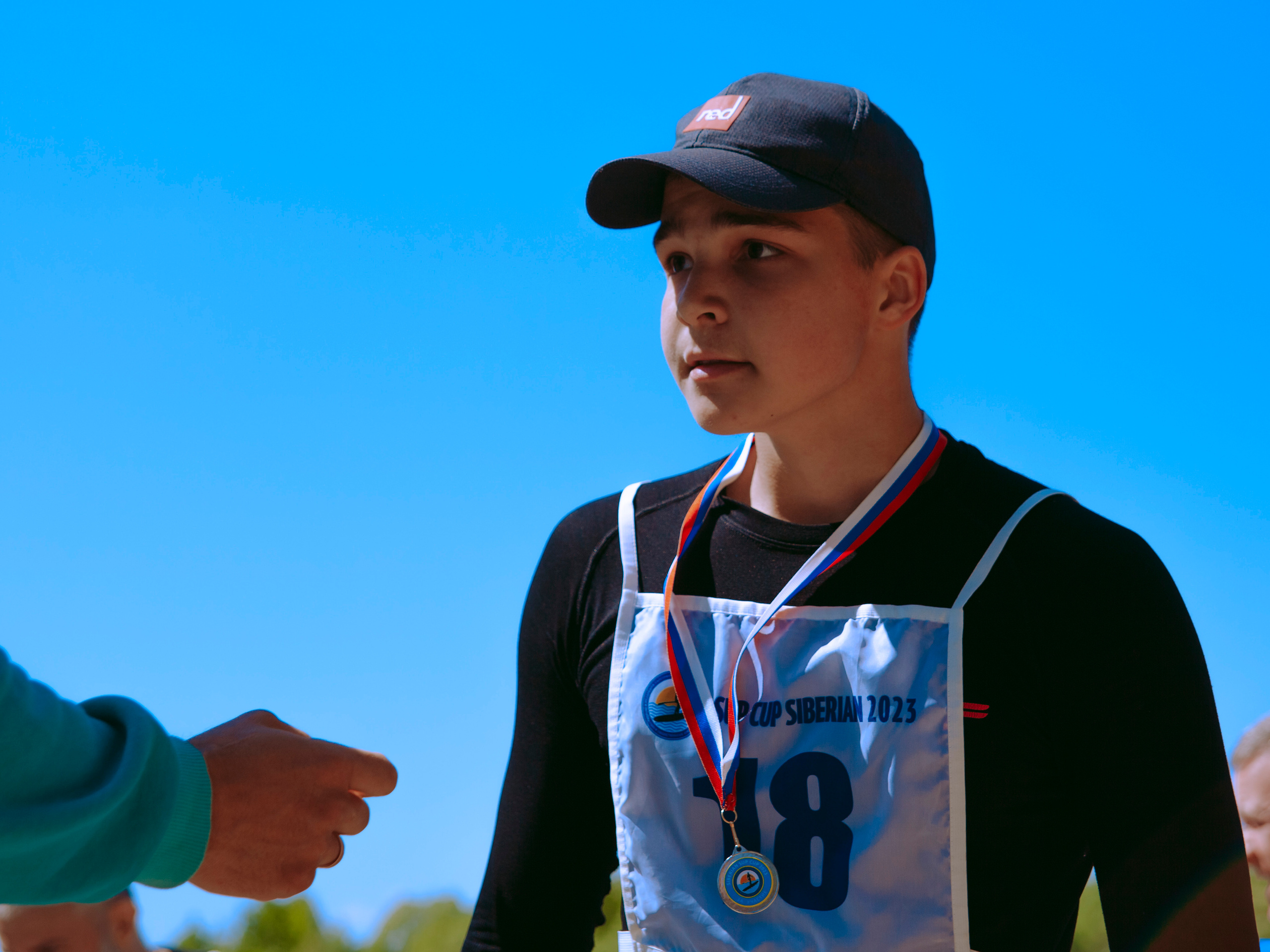 Парень в черном костюме в кепке и с медалью.